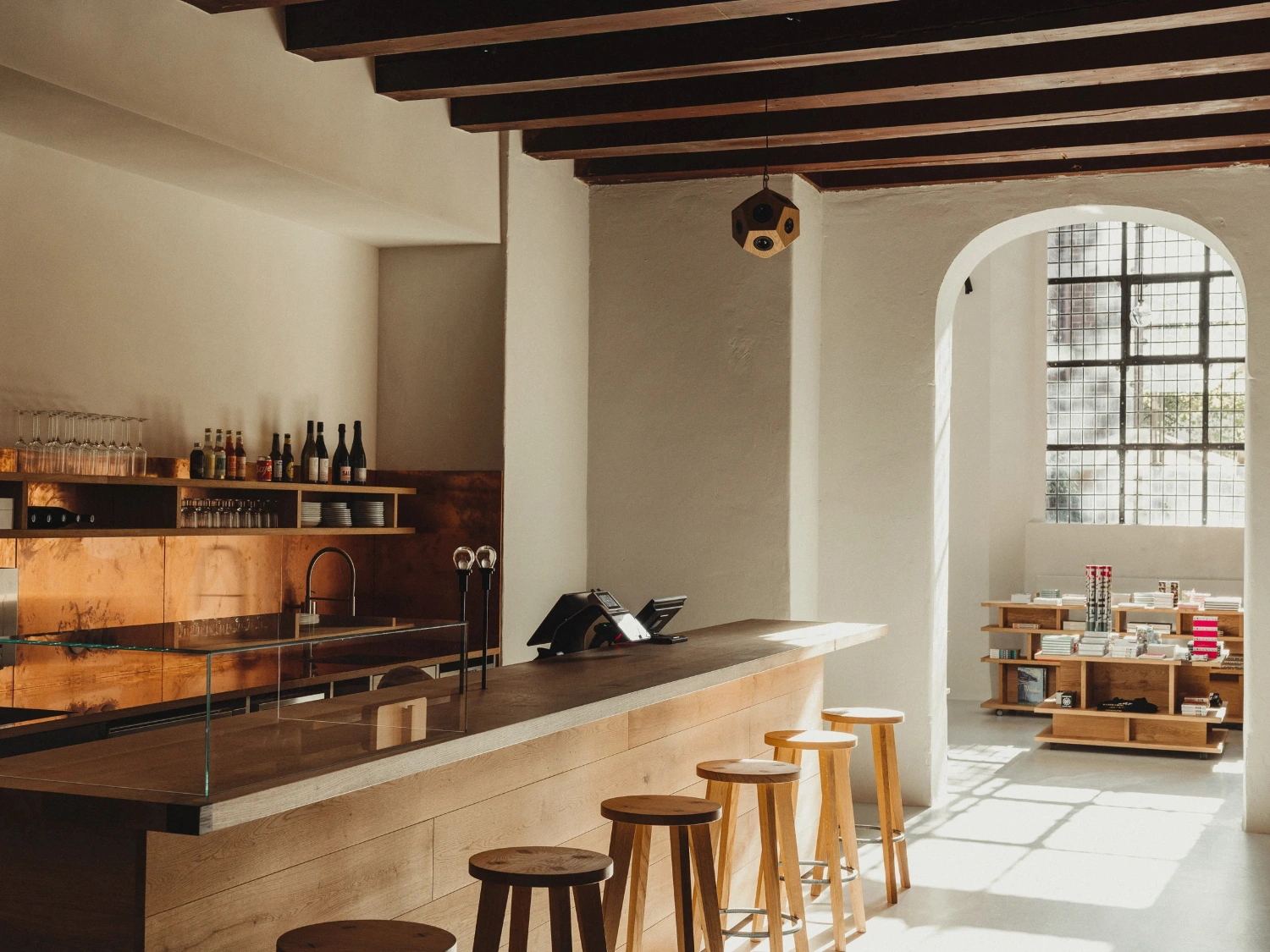 Nikolaj Kunsthal Café + Boutique by Engel Architects by MEE Studio — The café counter occupies the foreground as a linear datum, its pale timber edge contrasting with the dark stone work surface behind.
