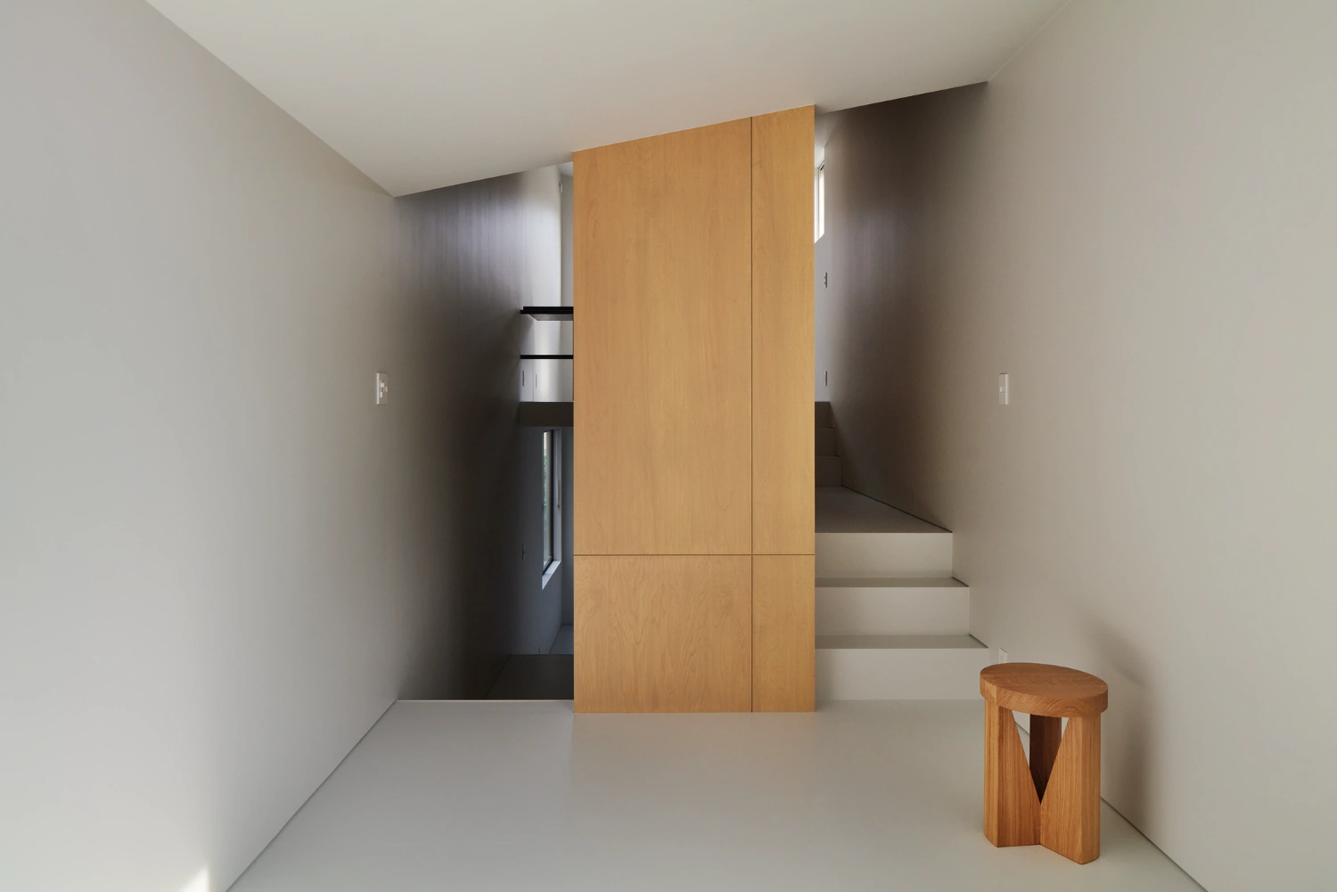 Retreat House by Arii Irie Architects — Interior passage defined by a monolithic oak-veneered partition wall with subtle vertical seam detailing, creating spatial compression within a...