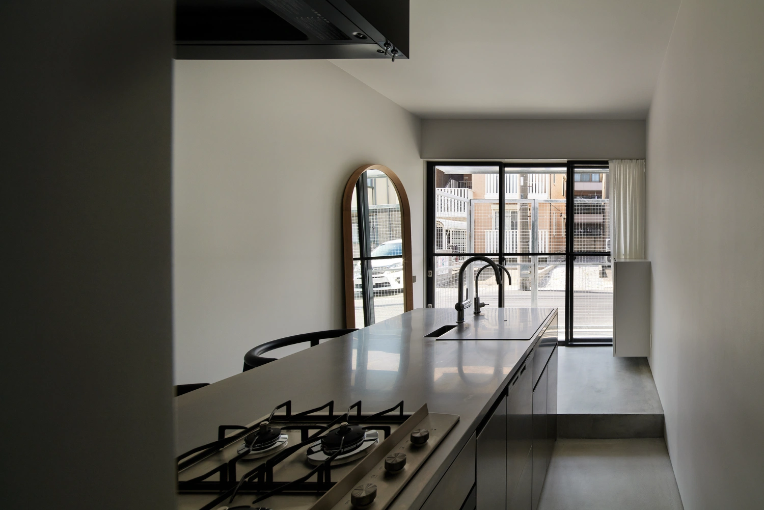 Retreat House by Arii Irie Architects — View through a contemporary kitchen toward expansive glazing framing urban context.
