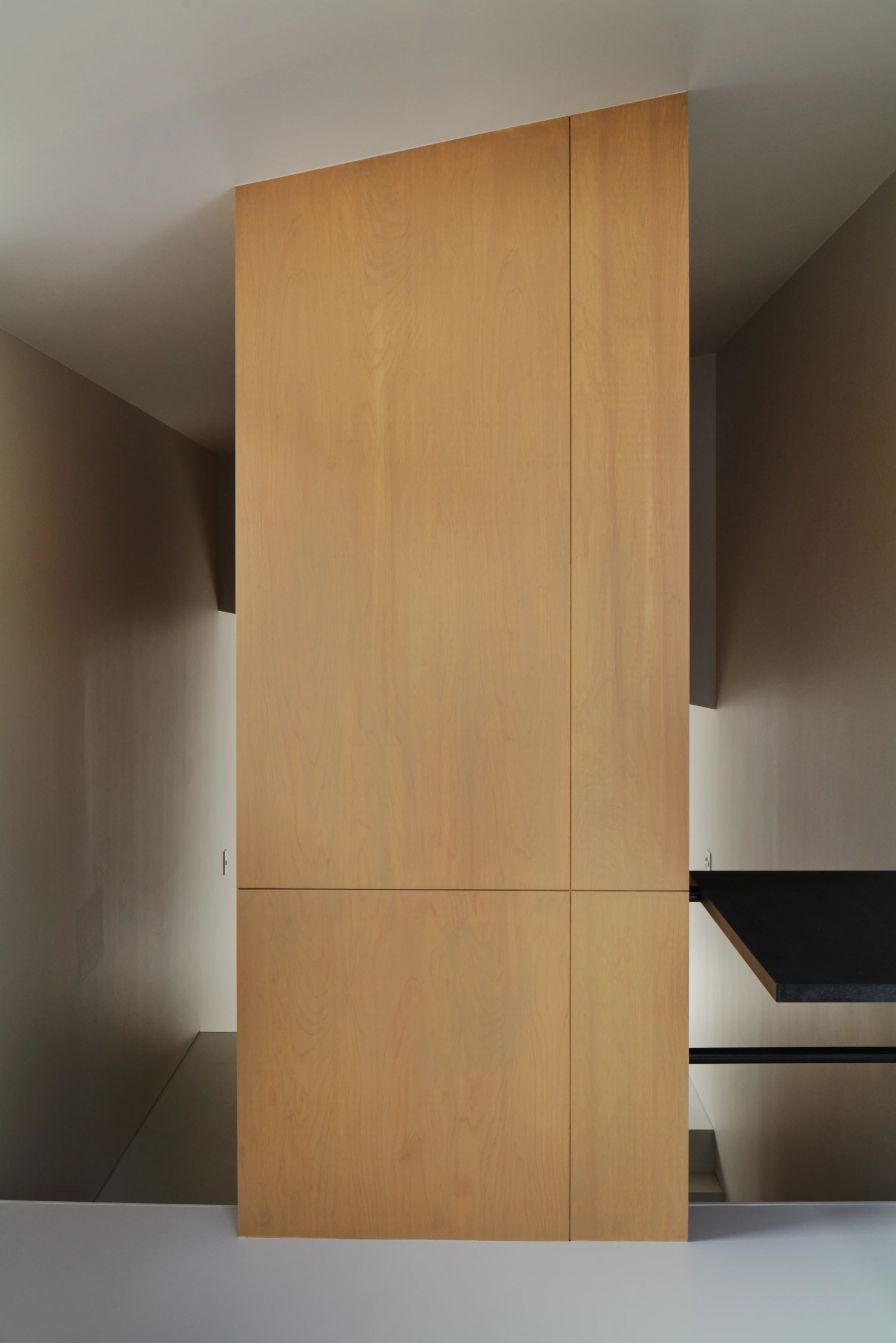 Retreat House by Arii Irie Architects — A monolithic timber door panel, rendered in light oak veneer, divides the interior threshold of the Retreat House.