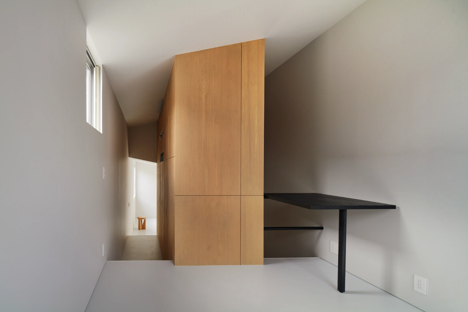 Retreat House by Arii Irie Architects — Interior passage framed by a monolithic timber partition wall in light oak, dividing the compact floor plan into distinct zones.