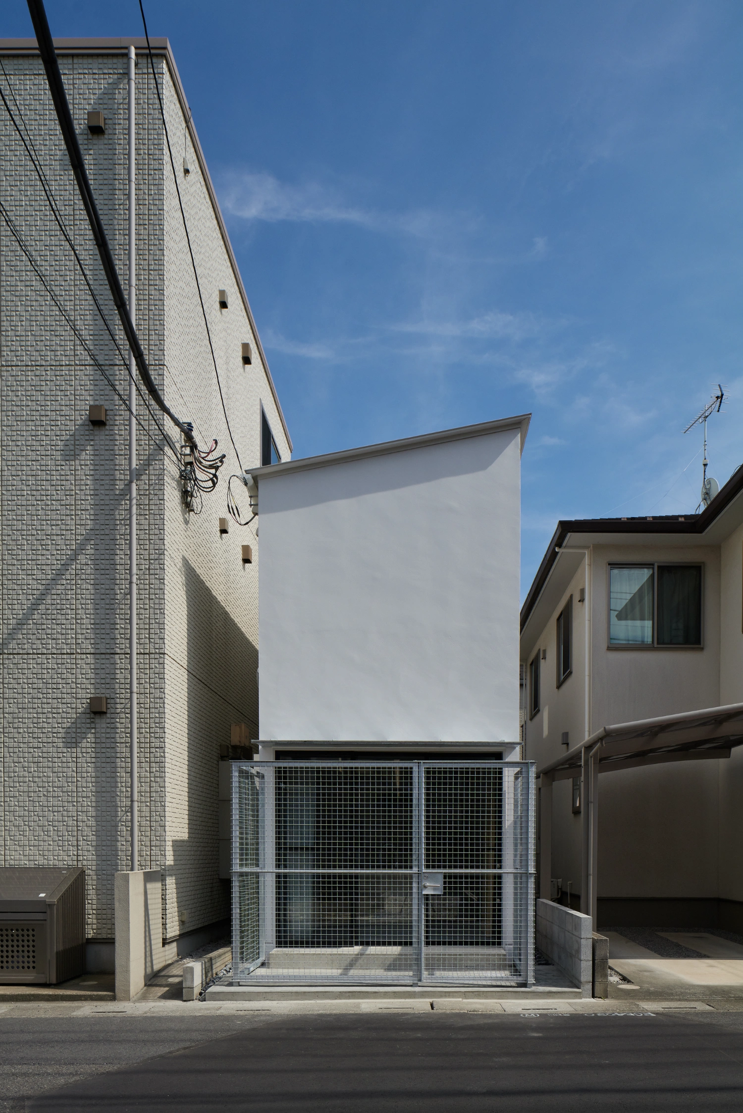 Retreat House by Arii Irie Architects — A compressed street facade presents a white rendered wall sandwiched between two brick structures, its geometric simplicity emphasized by flanking masonry.