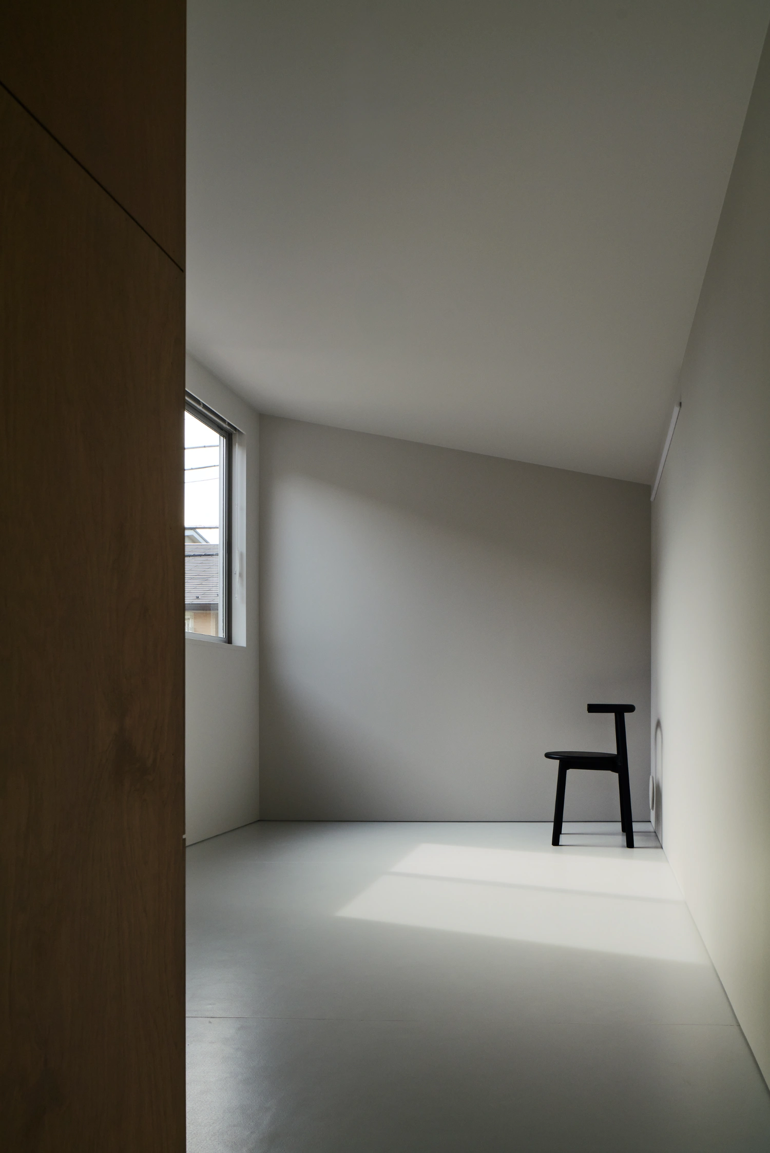 Retreat House by Arii Irie Architects — A minimal interior volume defined by white rendered walls and ceiling, flooded with directional daylight from a narrow horizontal window.