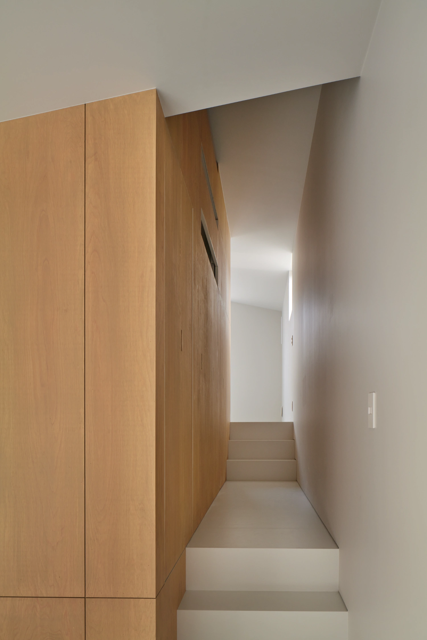 Retreat House by Arii Irie Architects — A narrow staircase ascending between a timber-clad wall on the left and white-rendered plaster on the right.
