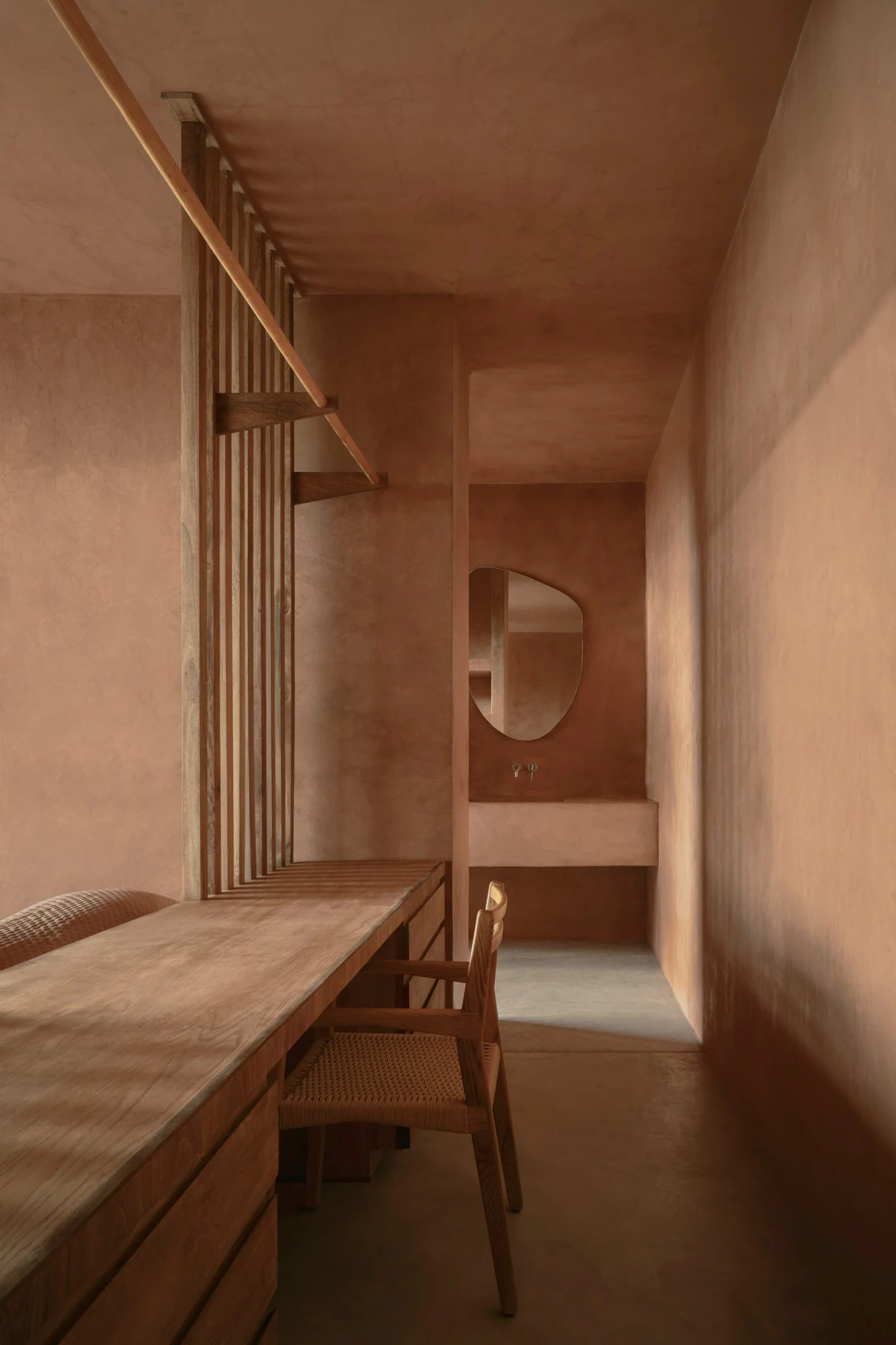 Casa Tobi by Espacio 18 Arquitectura — A narrow corridor rendered in terracotta plaster extends toward a vanity alcove, its monochromatic palette broken only by wooden elements.