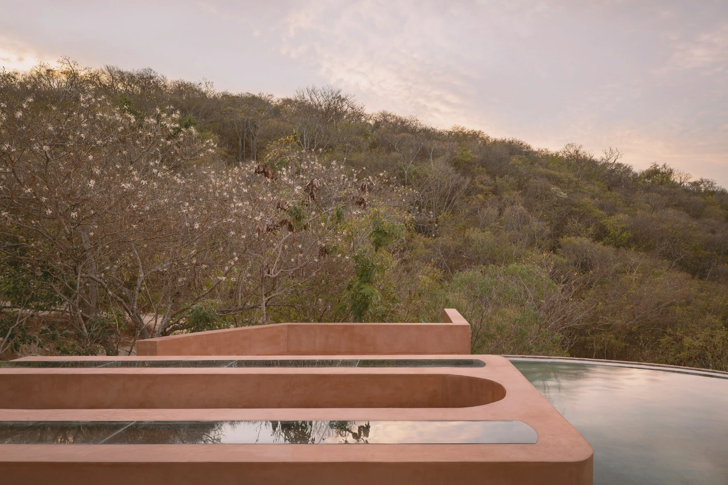 Casa Tobi by Espacio 18 Arquitectura — Casa Tobi's terracotta render facade dominates the composition, its cylindrical volumes stacked in horizontal tiers that step downward across the frame.