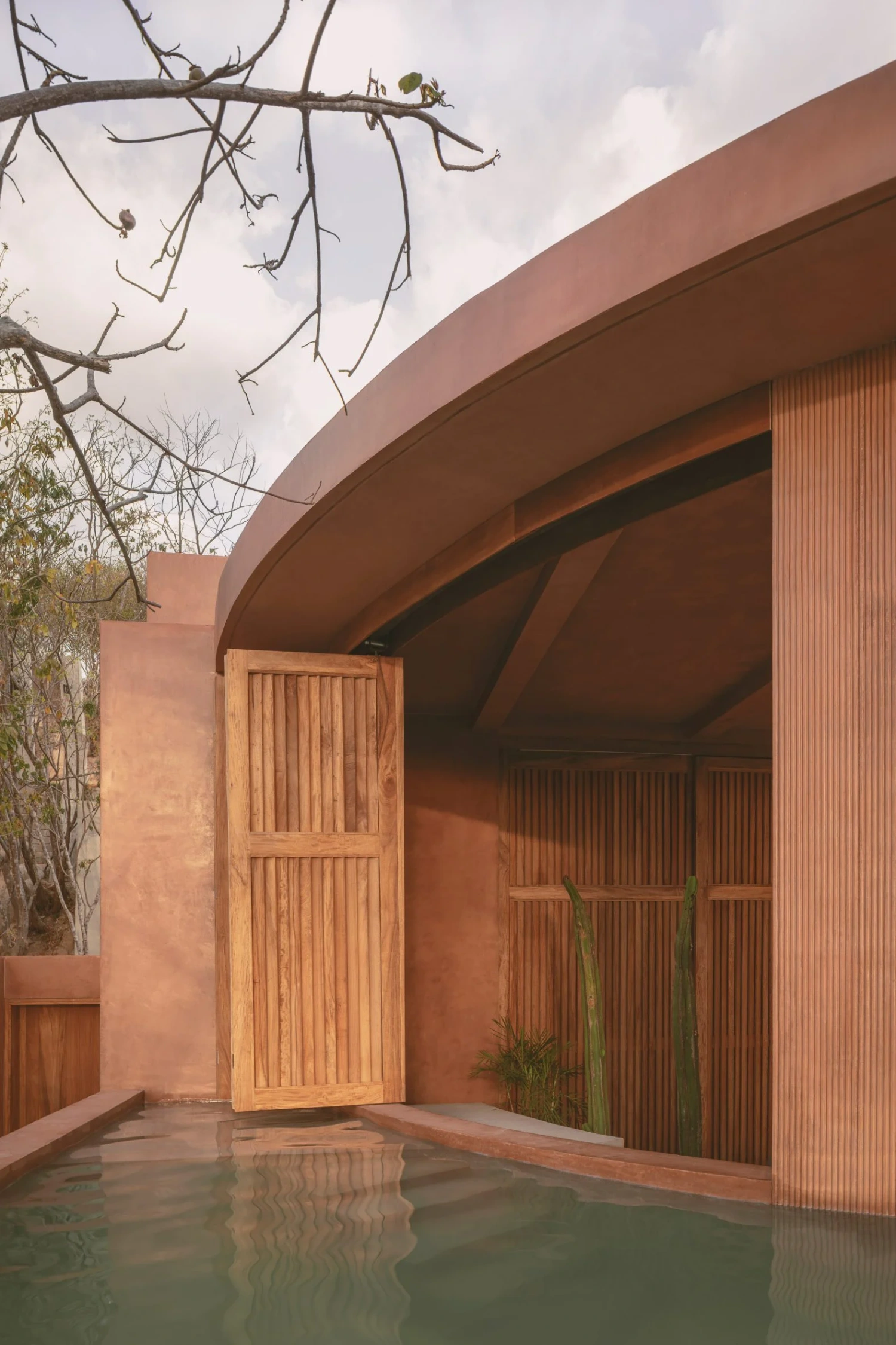 Casa Tobi by Espacio 18 Arquitectura — A terracotta-rendered cylindrical volume anchors the foreground, its curved roof form creating a dramatic overhang that frames the entrance.