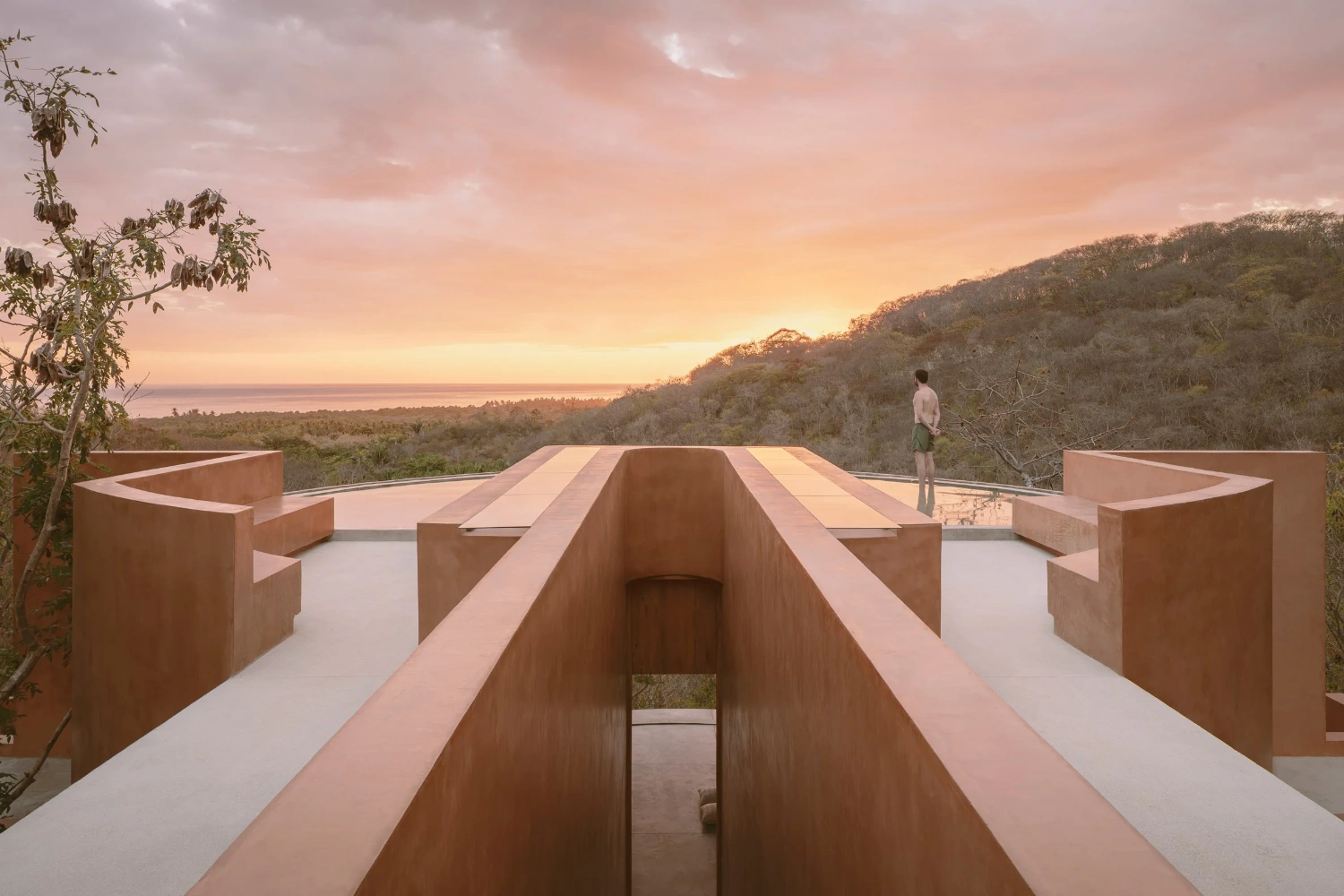 Casa Tobi by Espacio 18 Arquitectura — Golden-hour light bathes a terracotta-rendered architectural structure descending into an Oaxacan landscape.