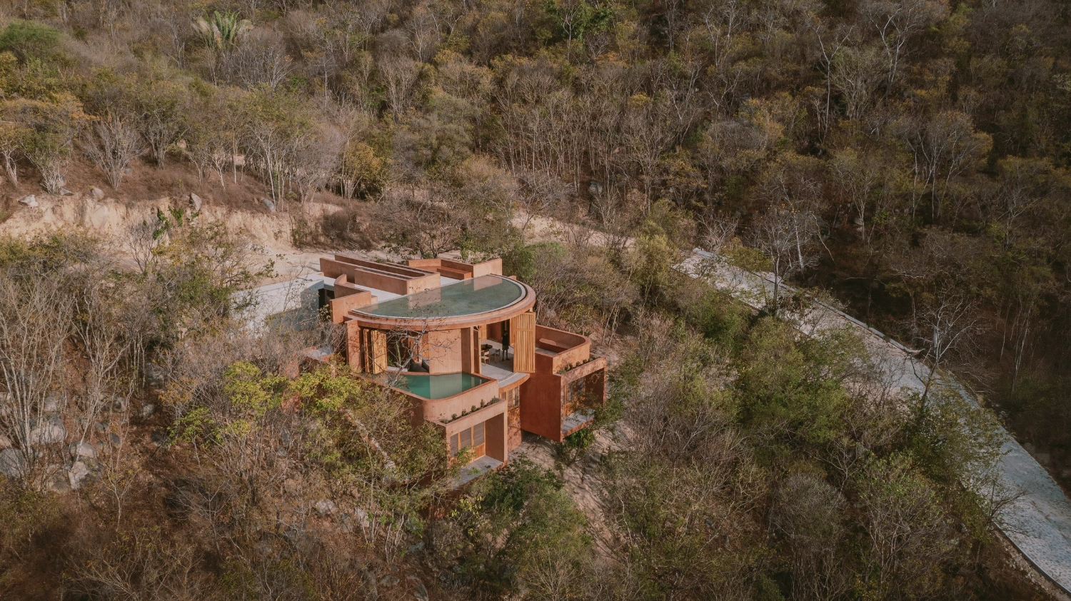Casa Tobi by Espacio 18 Arquitectura — Aerial perspective reveals Casa Tobi's stepped volumetric composition descending the hillside, its terracotta render surfaces responding to the sloping terrain.