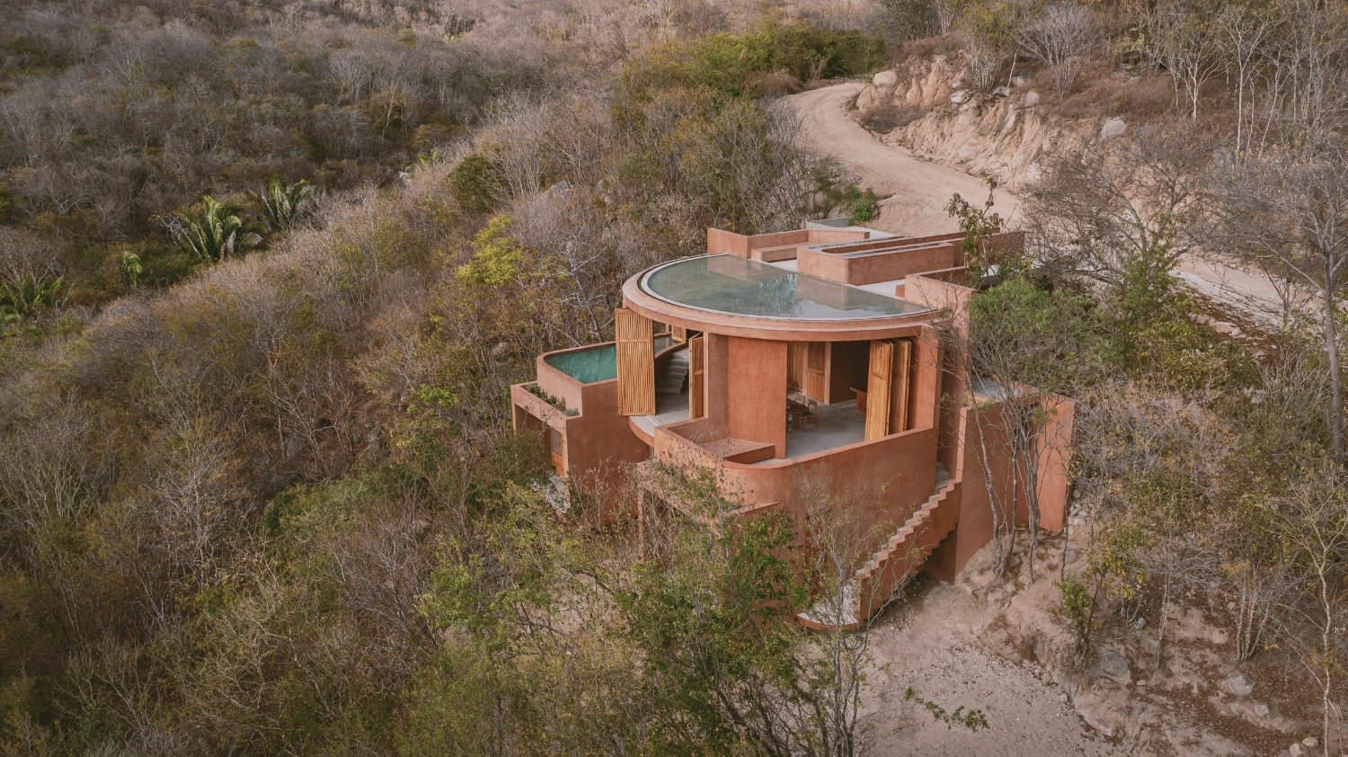Casa Tobi by Espacio 18 Arquitectura — Aerial view of Casa Tobi's cylindrical primary volume, its terracotta render rendered in warm rust tones against the sparse Oaxacan landscape.