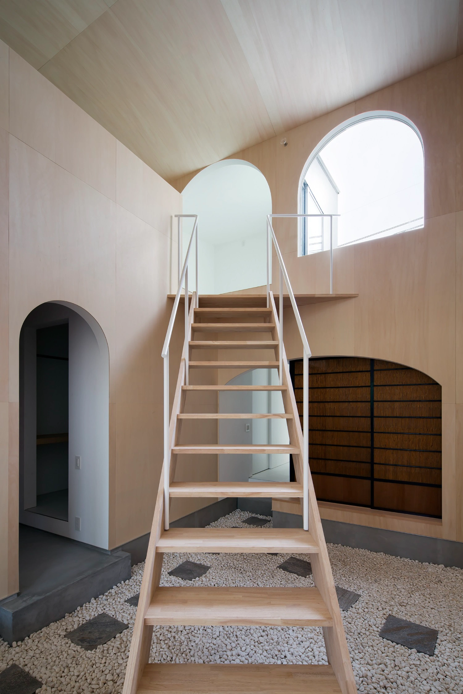 Courtyard in Kudamatsu by Container Design — A light-filled staircase ascends through a vaulted plywood interior, its diagonal timber treads supported by white steel railings and open stringers.
