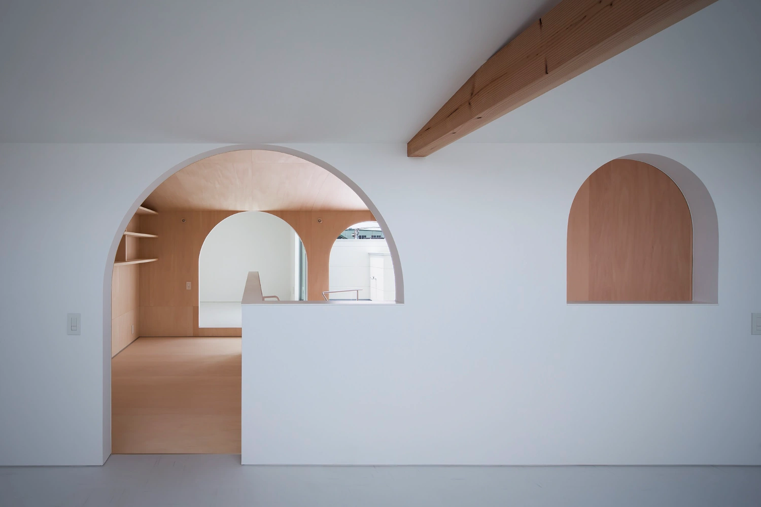Courtyard in Kudamatsu by Container Design — A volumetric passage unified by pale plywood surfaces and a barrel-vaulted ceiling that spans the full width of the frame.