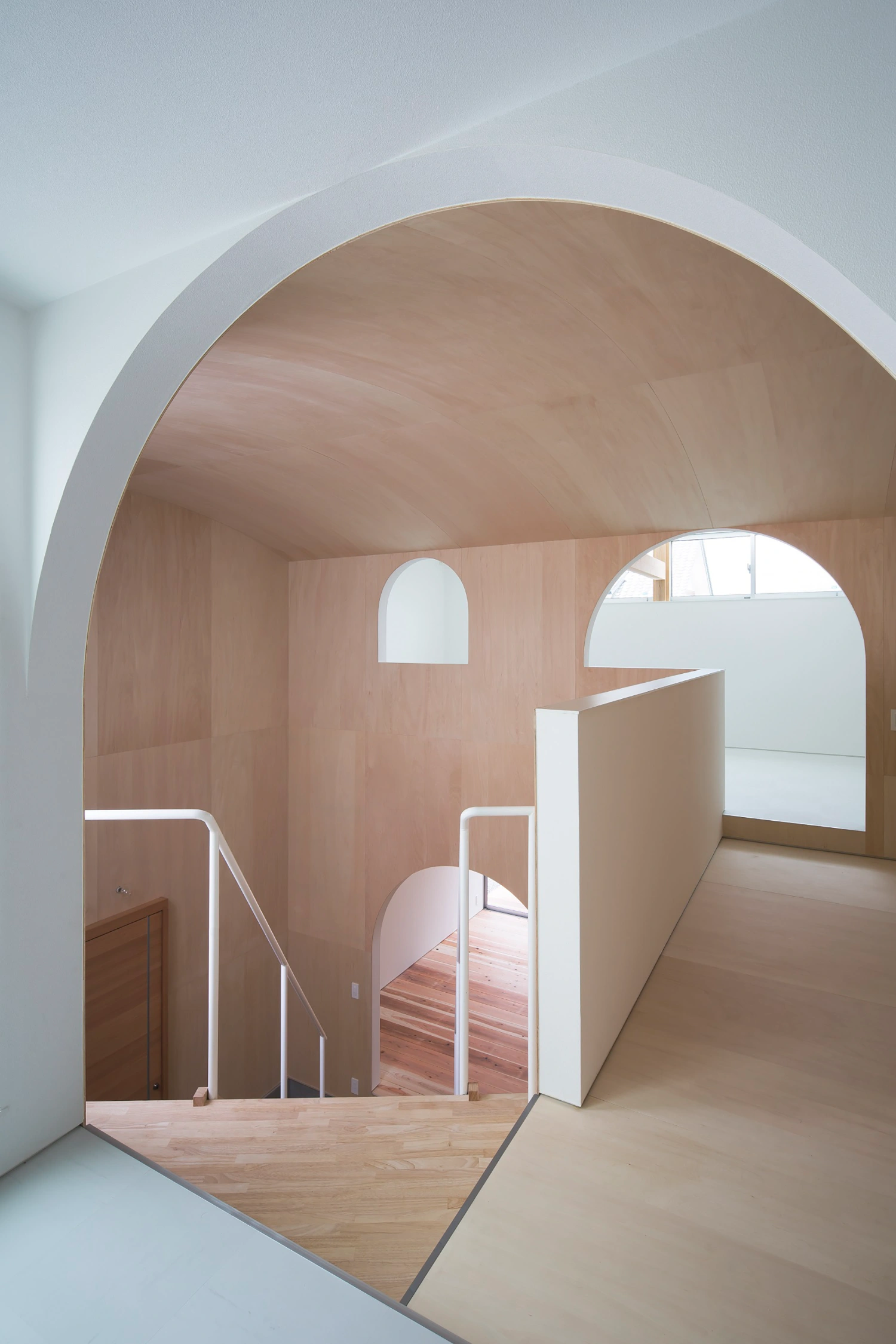 Courtyard in Kudamatsu by Container Design — A timber-lined passage articulated by a barrel-vaulted plywood ceiling that spans the full width, creating a volumetric envelope in warm beige tones.