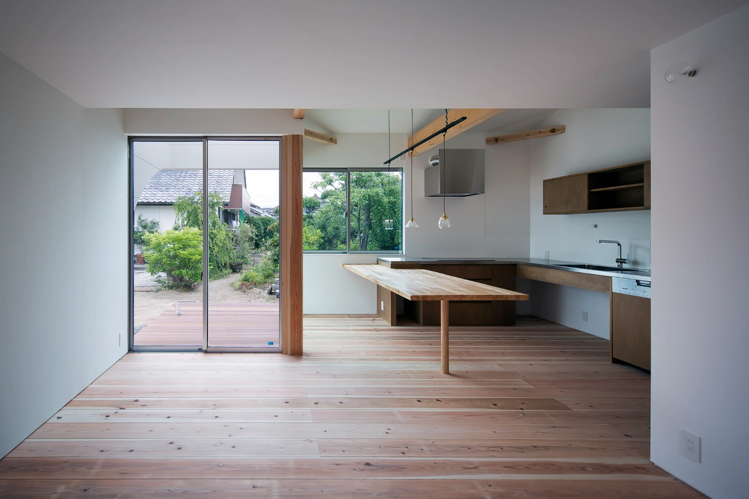 Courtyard in Kudamatsu by Container Design — An open-plan kitchen and dining volume unified by continuous timber flooring and a barrel-vaulted plywood ceiling that spans the full width.
