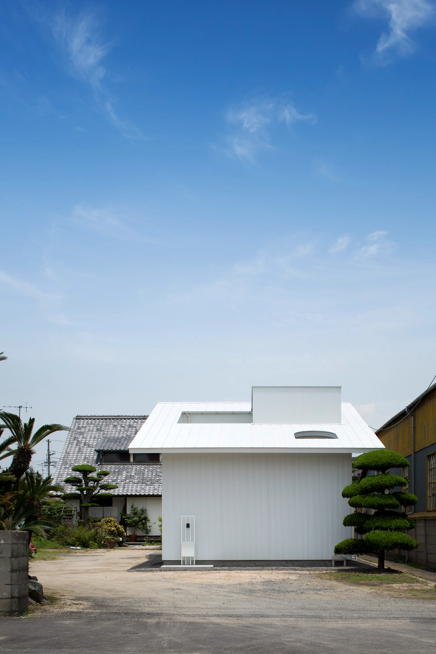Courtyard in Kudamatsu by Container Design — The white corrugated metal facade of Courtyard in Kudamatsu presents a geometric volume fronting the residential plot in Yamaguchi.