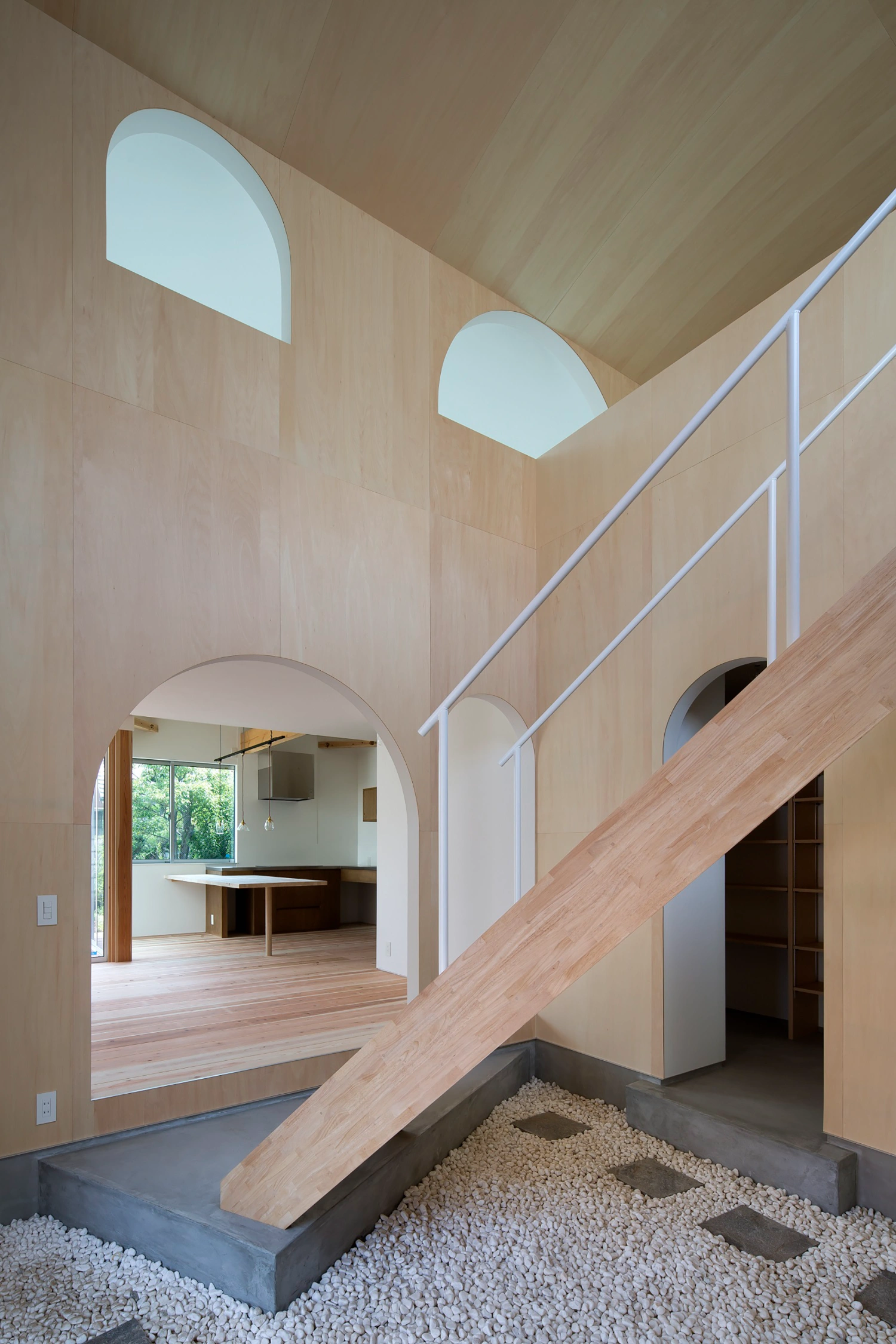 Courtyard in Kudamatsu by Container Design — A timber staircase dominates the central volume, its diagonal trajectory cutting through a unified plywood interior.