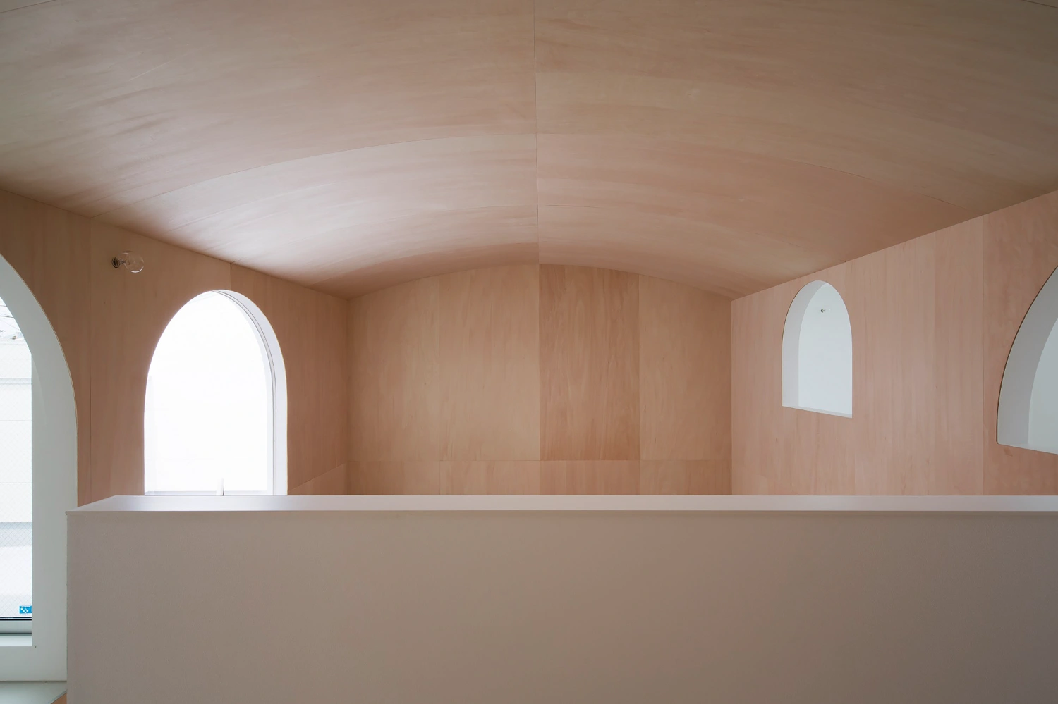 Courtyard in Kudamatsu by Container Design — The barrel-vaulted plywood ceiling dominates this upper passage, its curved form spanning the full width in continuous pale timber panels.