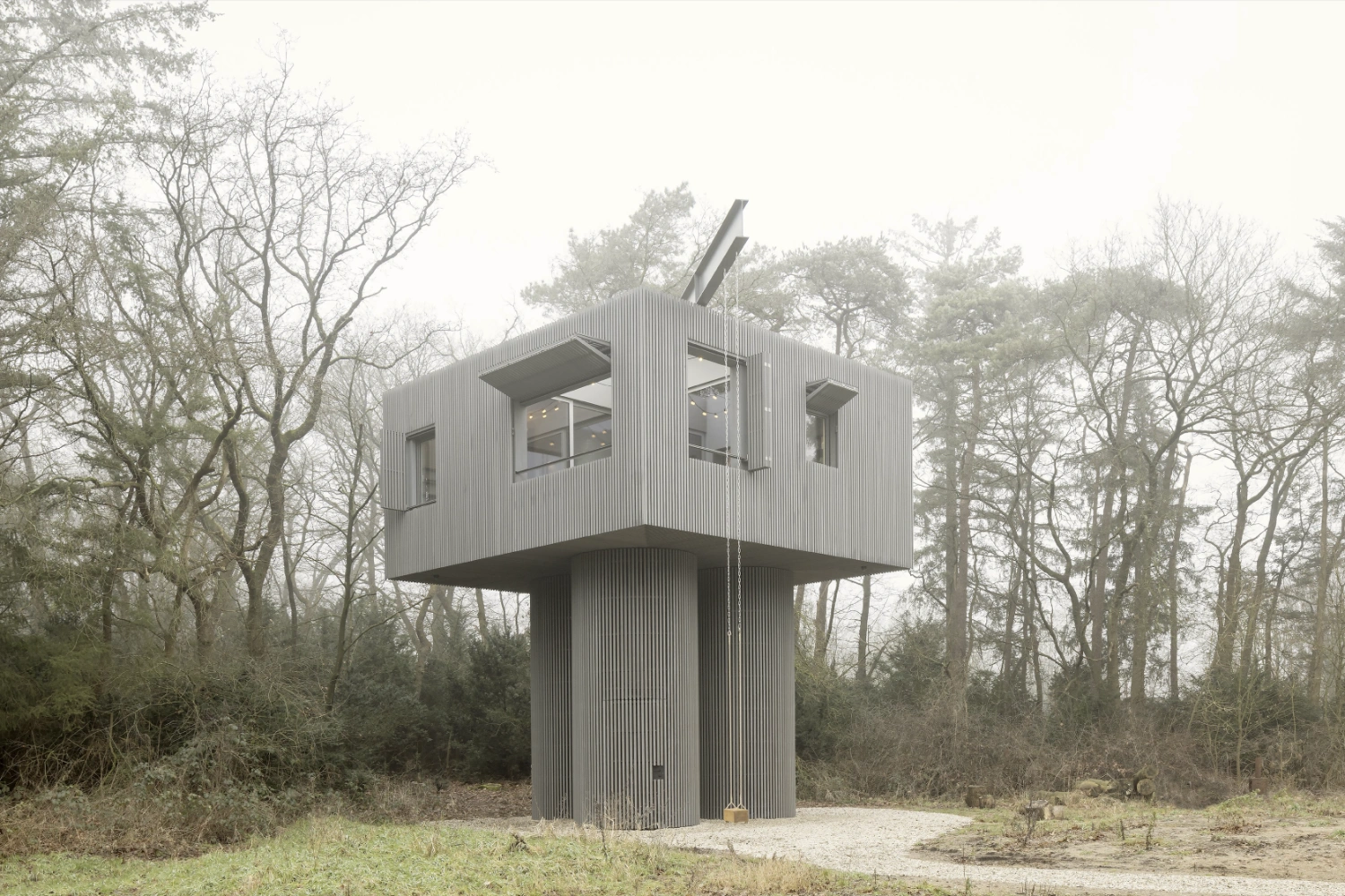 Dolmen by Space Encounters — A cylindrical three-legged tower rises from a forest clearing in Arnhem, its cubic upper chamber clad in vertical corrugated metal that catches diffuse...