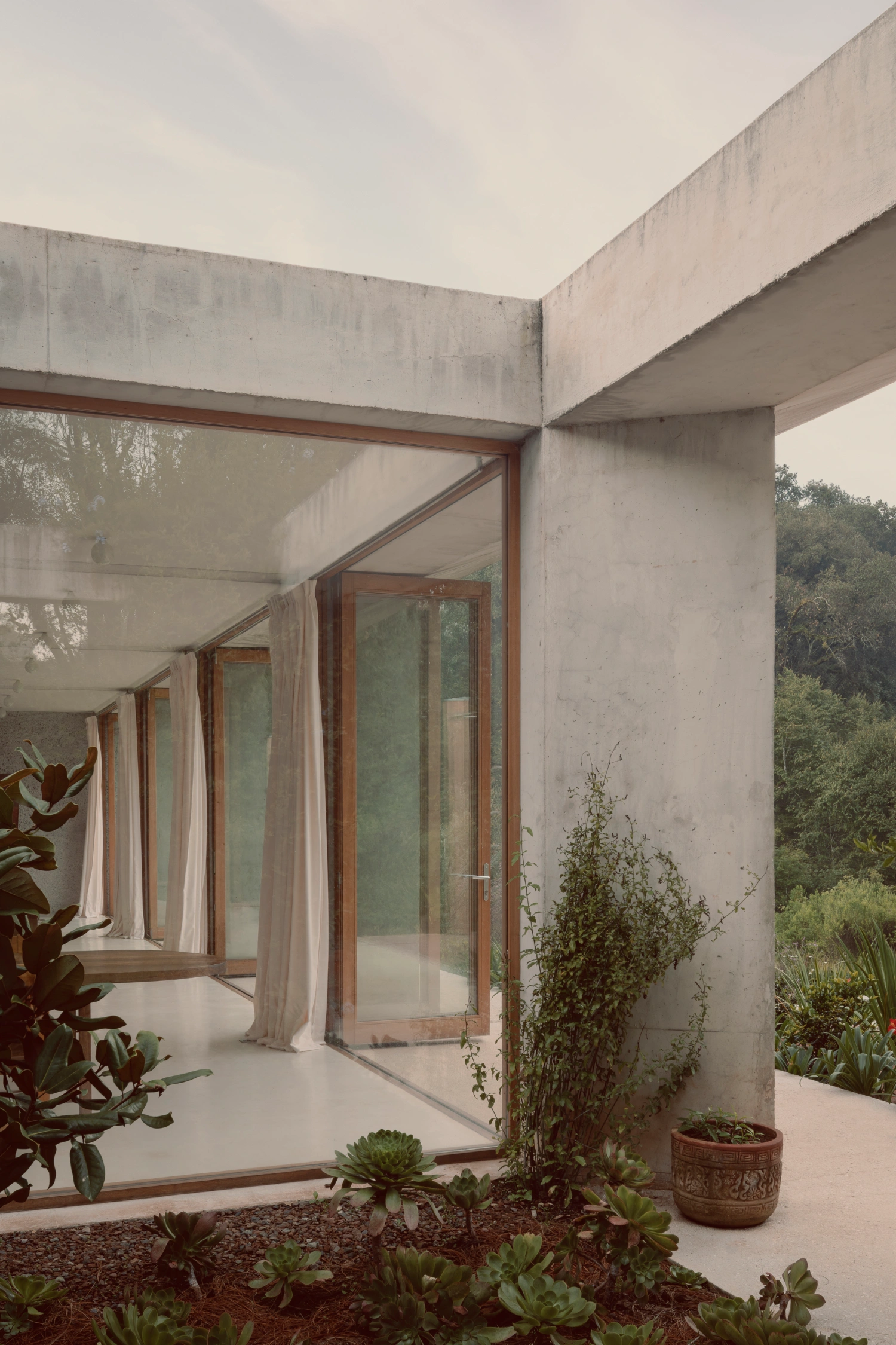 House Between Two Rivers by Taller 3000 — A rendered concrete terrace unfolds beneath a monolithic cantilevered beam, its horizontal mass casting shadow across the threshold.
