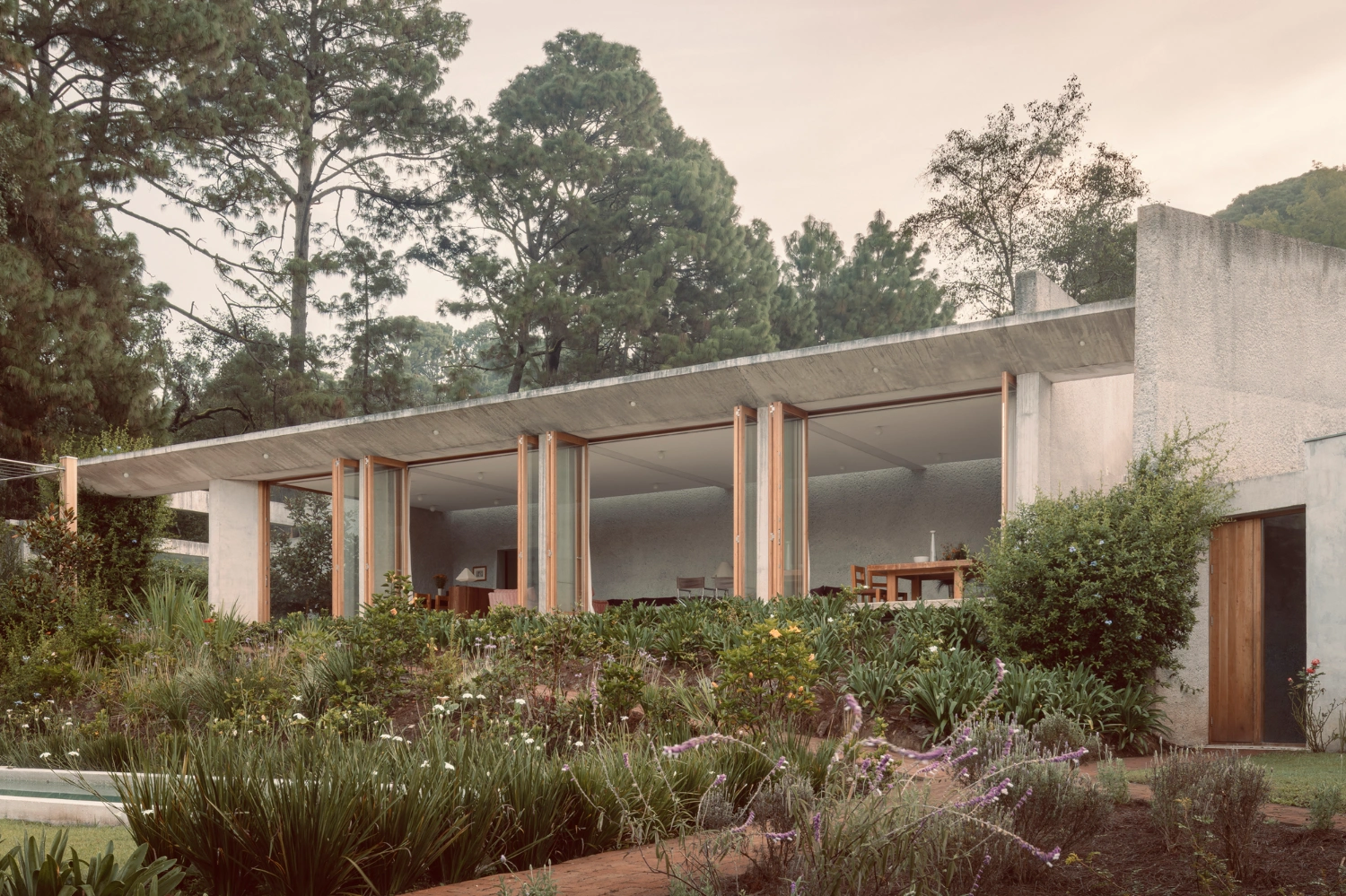 House Between Two Rivers by Taller 3000 — The house presents itself as a horizontal datum across the hillside, its monolithic concrete structure anchored by a massive cantilevered beam that extends...