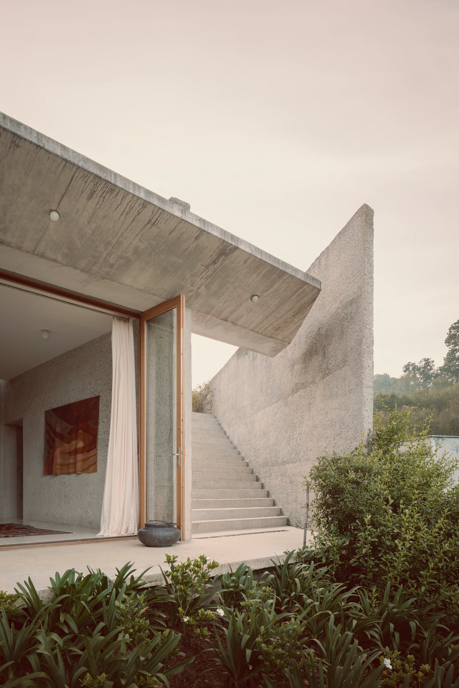 House Between Two Rivers by Taller 3000 — The threshold between interior and landscape is mediated by a monumental concrete cantilever and an angled wall plane that cuts diagonally across the frame.