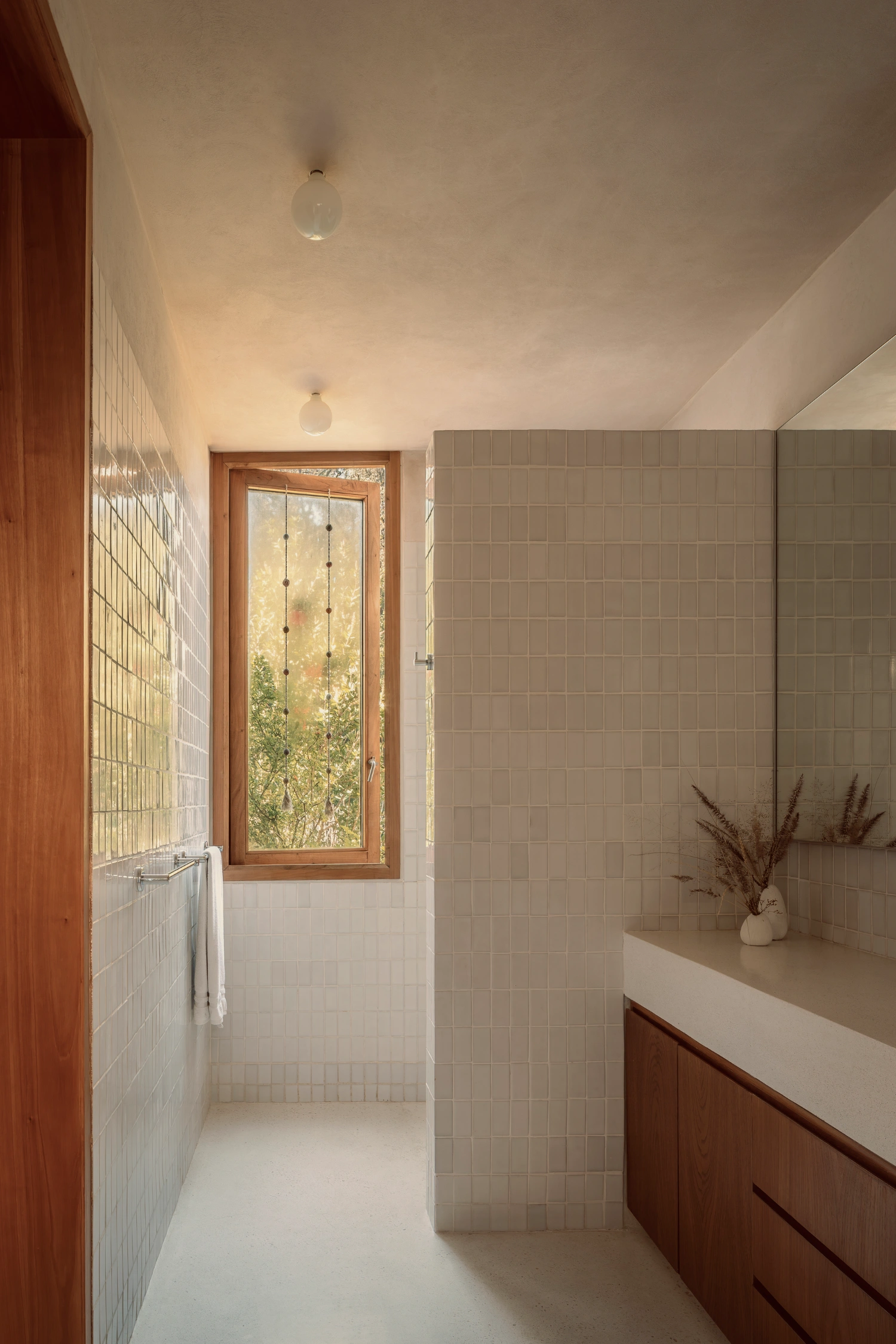House Between Two Rivers by Taller 3000 — A narrow bathroom corridor lined with small square ceramic tiles in warm grey-beige, punctuated by two pendant lights suspended from a white ceiling.