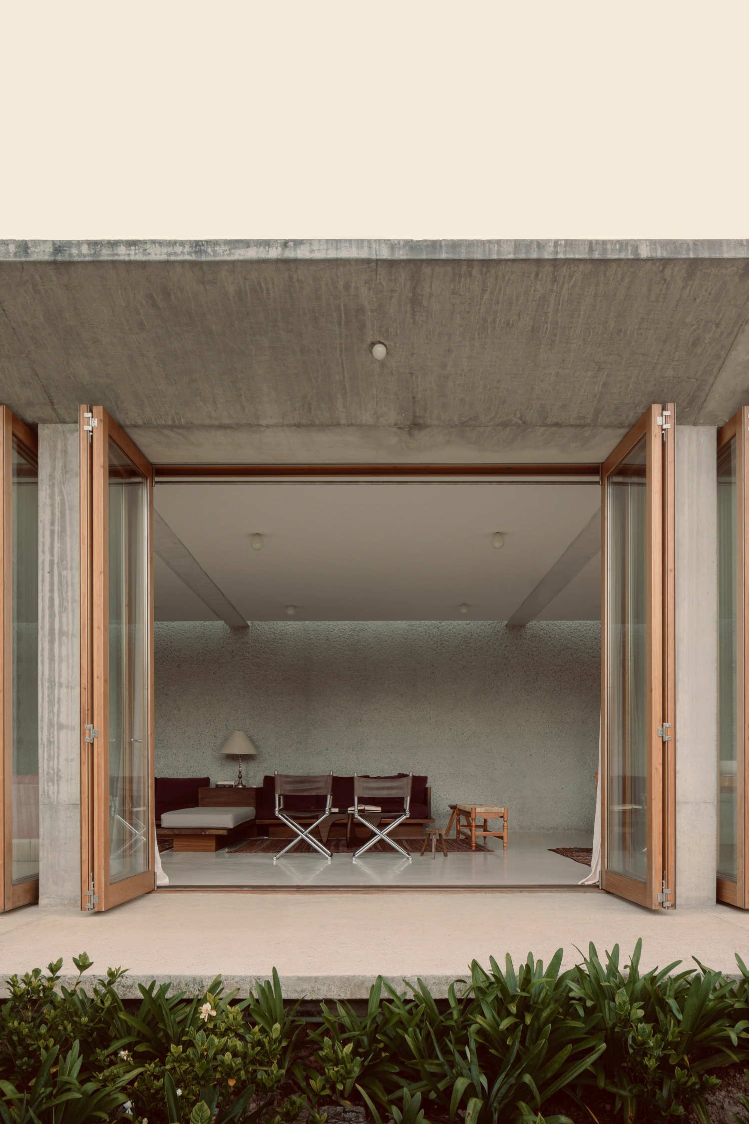 House Between Two Rivers by Taller 3000 — A monumental timber-framed glass threshold opens onto a rendered concrete interior, the sliding doors held open to reveal a burgundy leather sectional and...