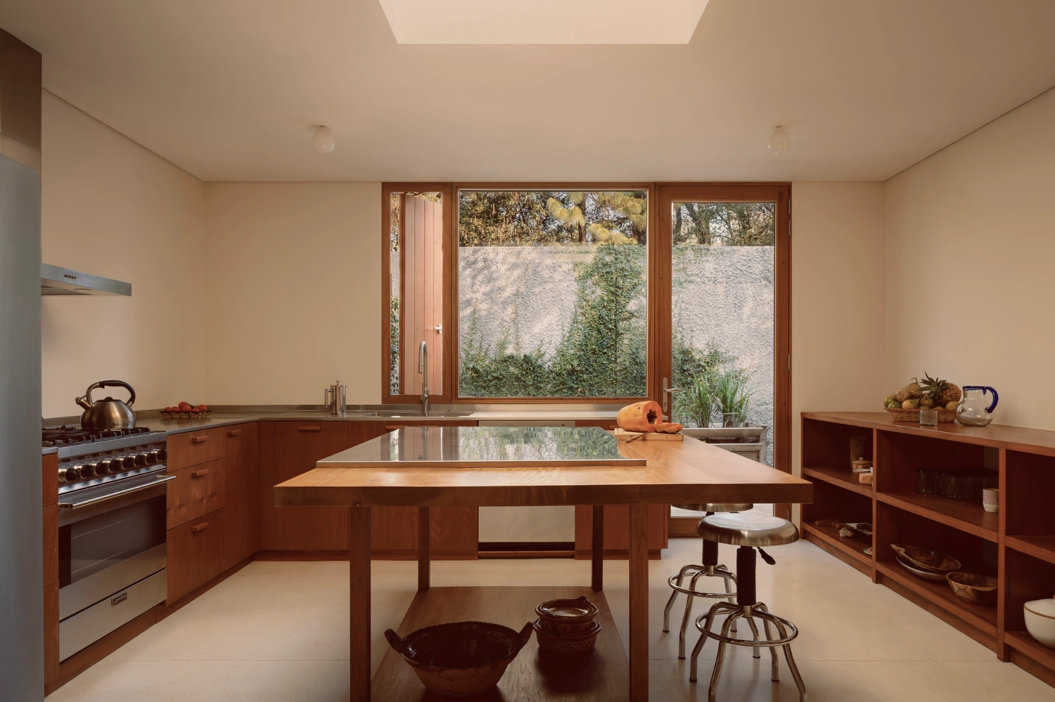 House Between Two Rivers by Taller 3000 — The kitchen interior reveals the project's material and spatial logic through walnut cabinetry, rendered concrete surfaces, and large glazed openings...