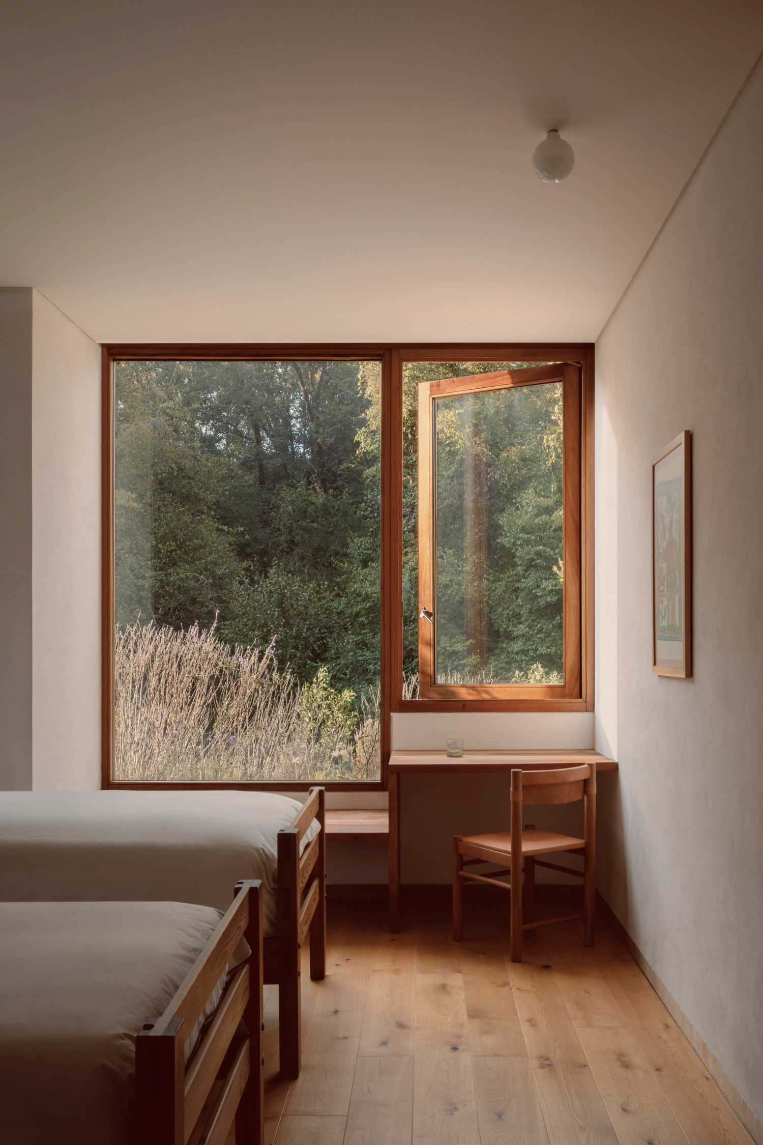 House Between Two Rivers by Taller 3000 — A bedroom interior featuring twin beds with timber frames positioned along the left wall, their pale bedding contrasting with the warm wood construction.