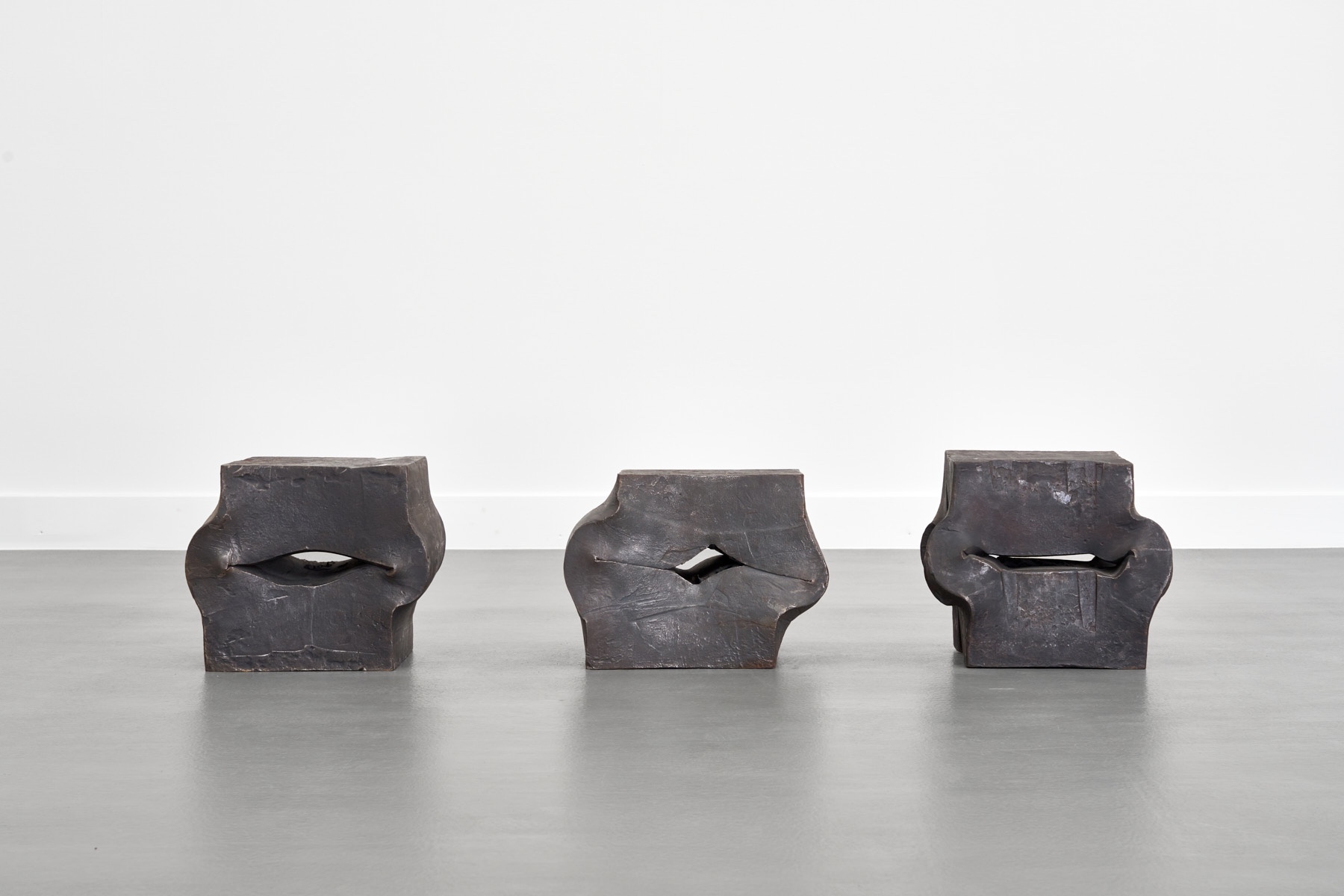 Materie Stahl by Alf Lechner at Lechner Museum — Three cast-bronze sculptural forms arranged in frontal alignment on polished concrete.