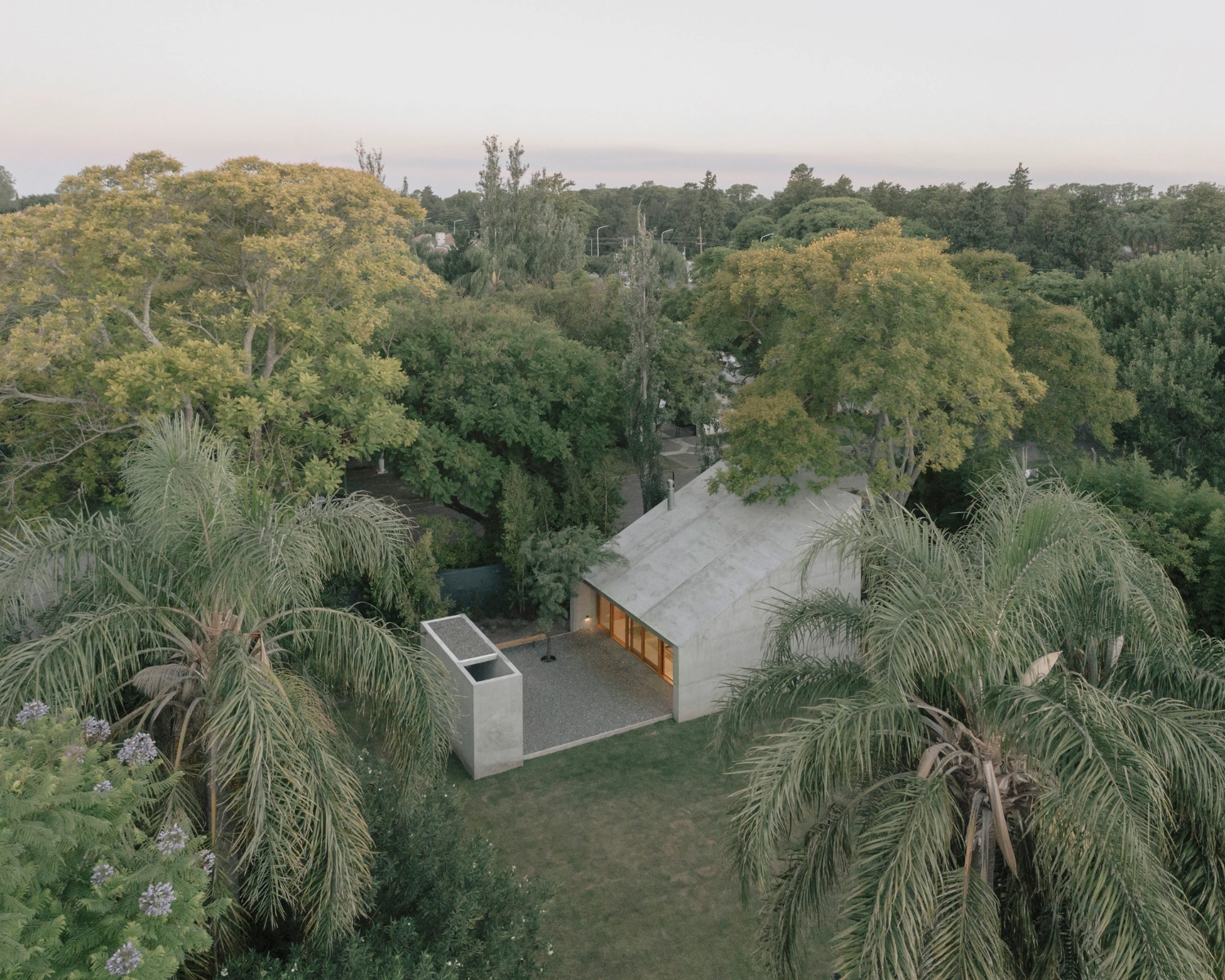 Atelier Workshop by Agustín Berzero — Aerial perspective reveals the workshop's recessed insertion within dense tree canopy, its monolithic concrete slab roof appearing as a horizontal datum...