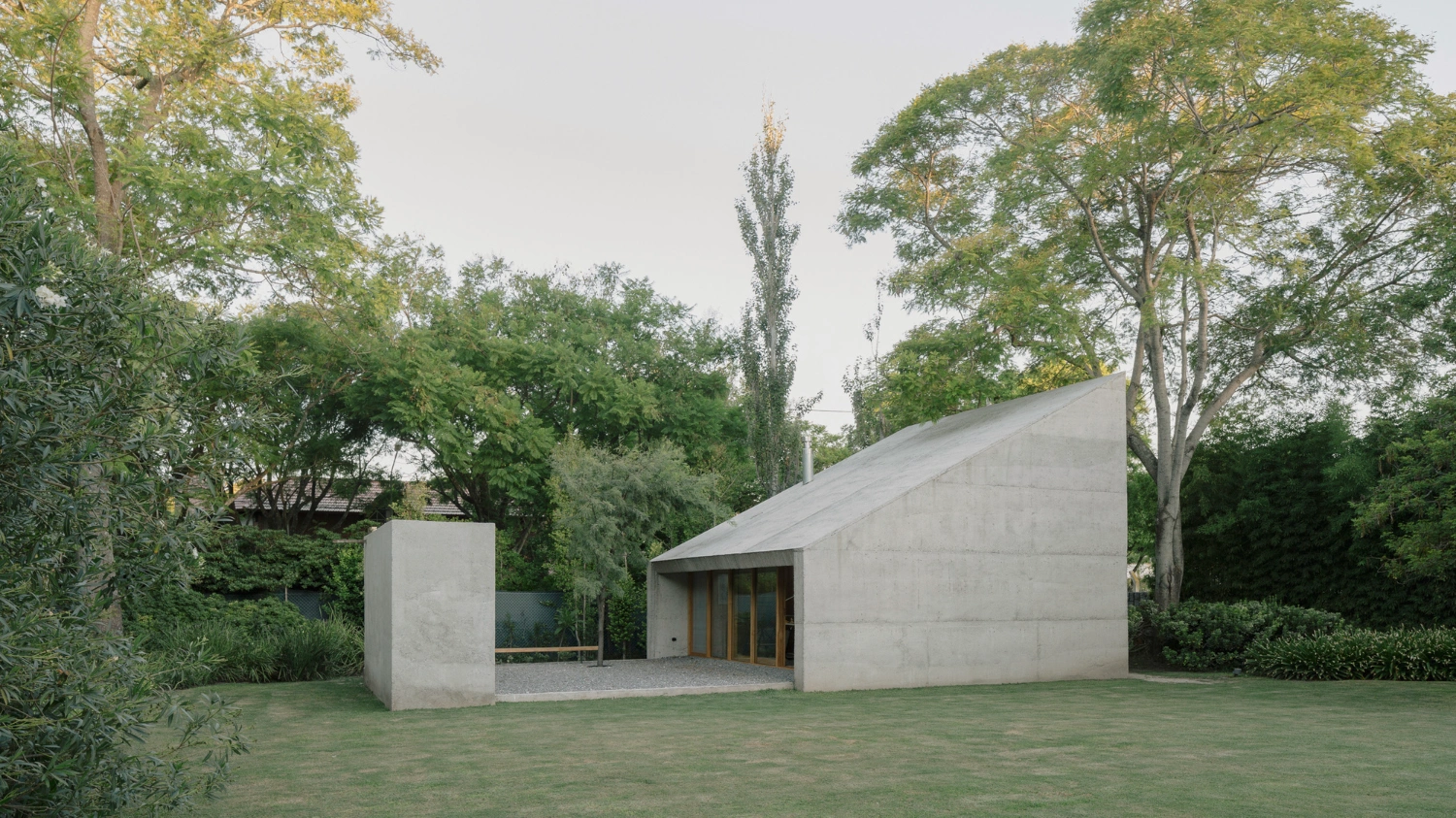 Atelier Workshop by Agustín Berzero — A monolithic concrete workshop emerges from its forest setting as two rectilinear volumes—a pitched-roof main structure paired with a cylindrical concrete...