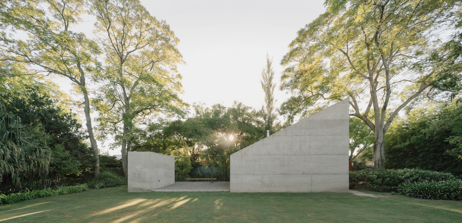 Atelier Workshop by Agustín Berzero — Two monolithic concrete volumes define a recessed courtyard within a mature tree canopy.