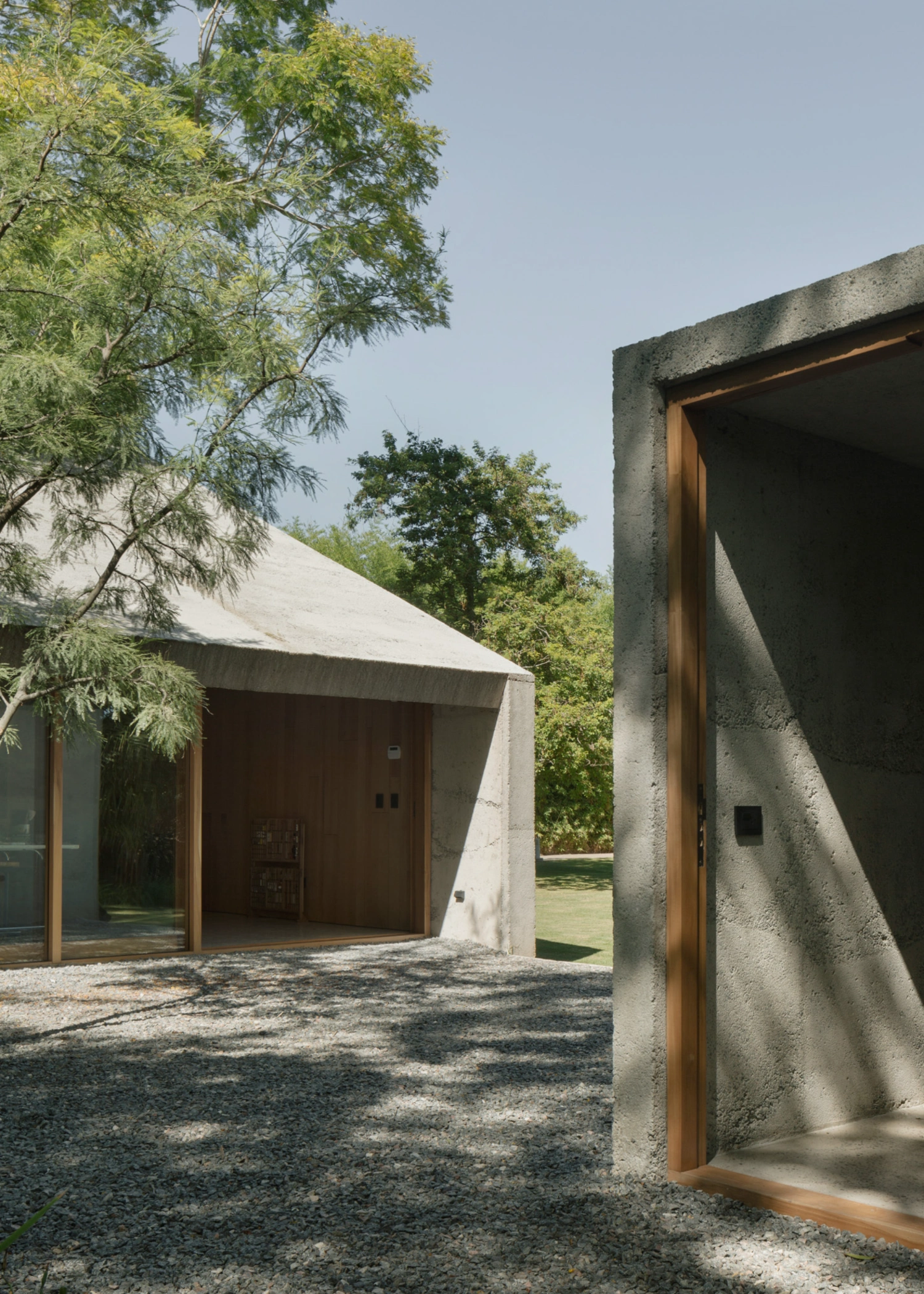 Atelier Workshop by Agustín Berzero — A timber-framed concrete portal frames the gravel courtyard in sharp relief, its warm wood trim glowing against raw grey concrete.