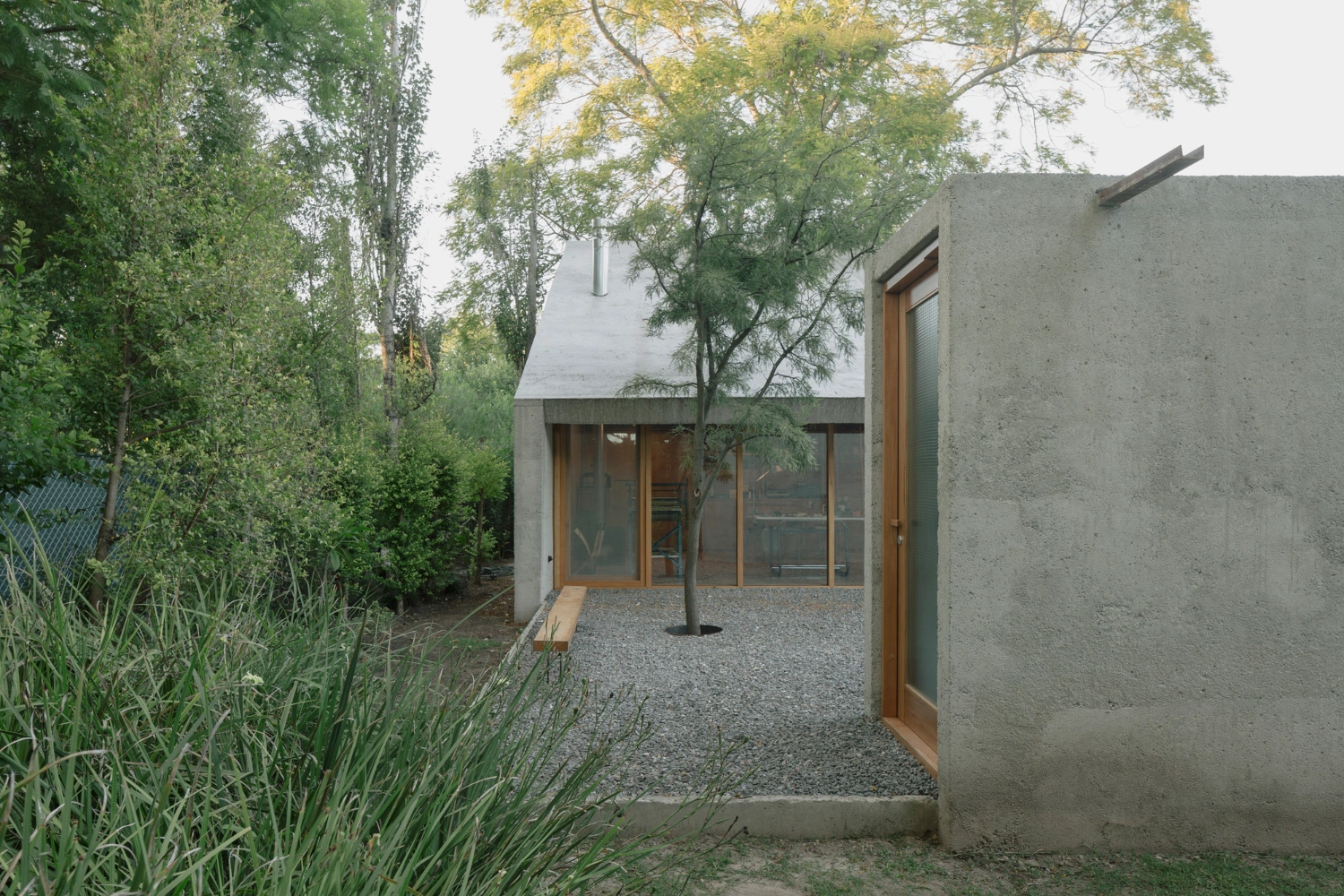 Atelier Workshop by Agustín Berzero — The entrance courtyard reveals the project's spatial economy: a monolithic concrete volume recessed within dense vegetation, its raw material surface...