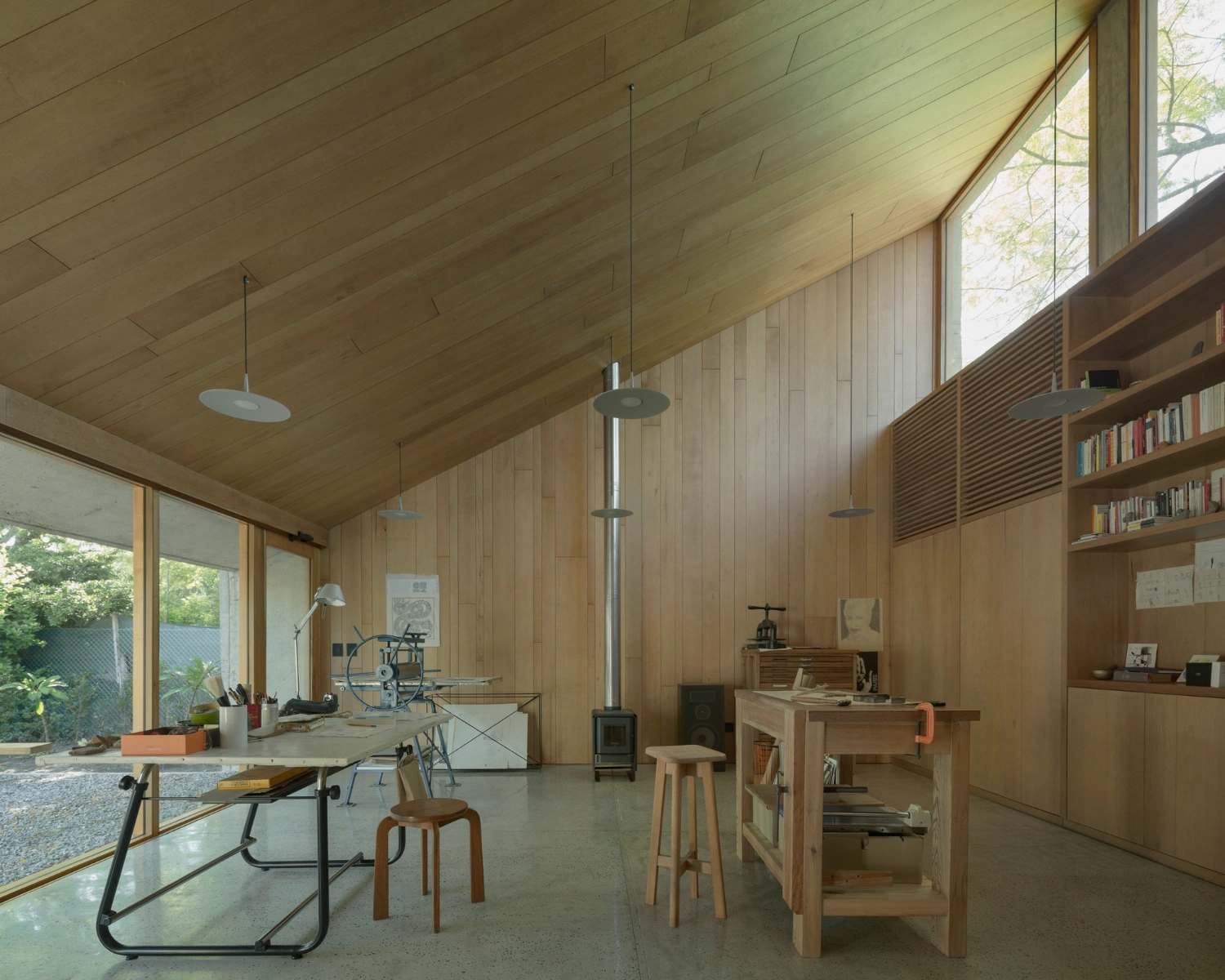 Atelier Workshop by Agustín Berzero — Interior view of the timber-lined workshop reveals a dual-desk configuration positioned perpendicular to the glazing strip, establishing distinct work zones...