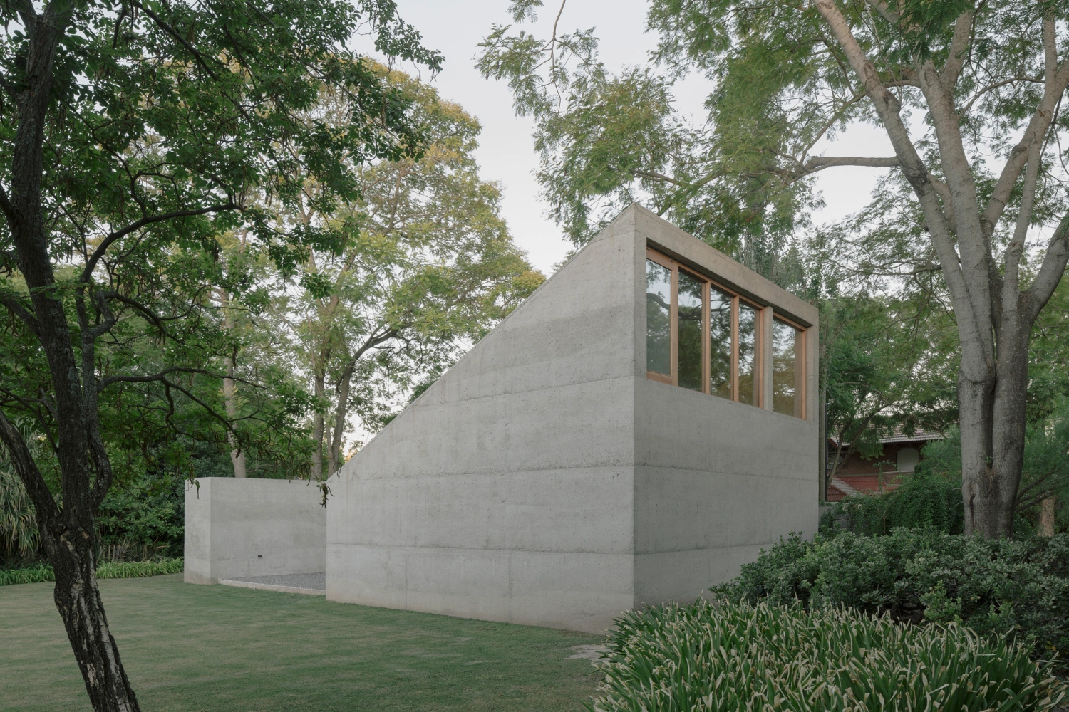 Atelier Workshop by Agustín Berzero — A monolithic concrete volume sits recessed within a mature tree canopy, its raw board-formed surfaces rendered in grey.