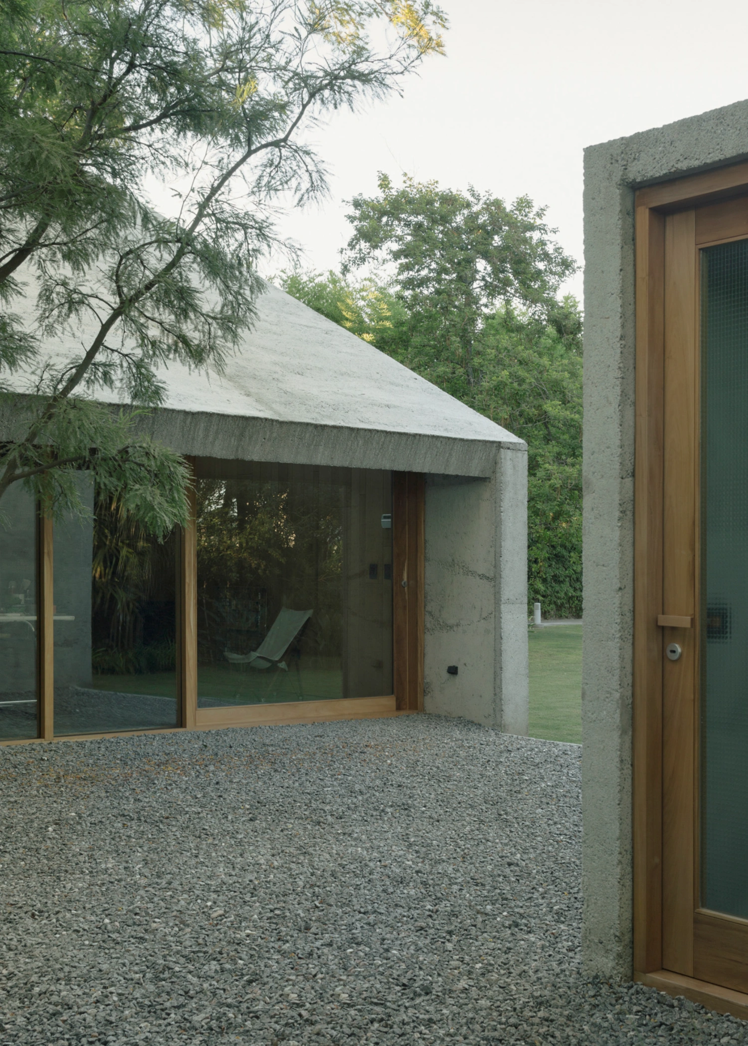 Atelier Workshop by Agustín Berzero — The workshop's southern elevation presents a singular glazed opening framed in timber, its warm wood tone contrasting the monolithic concrete wall.