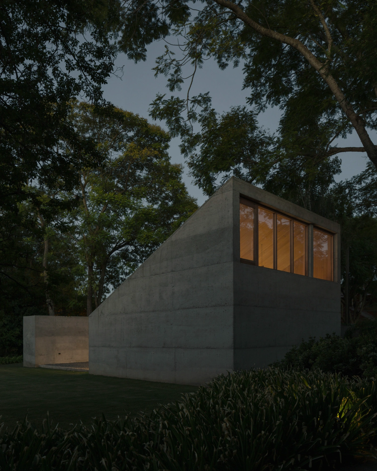 Atelier Workshop by Agustín Berzero — A monolithic concrete workshop sits recessed within dense tree canopy, its planar geometries asserting geometric clarity against organic surroundings.