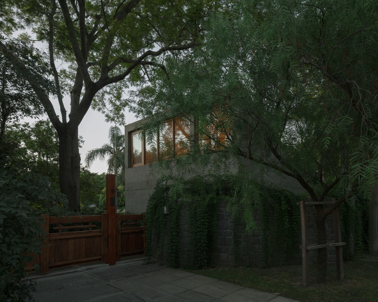 Atelier Workshop by Agustín Berzero — A concrete-block workshop emerges from dense vegetation, its monolithic form partially obscured by weeping willow fronds that frame the foreground.
