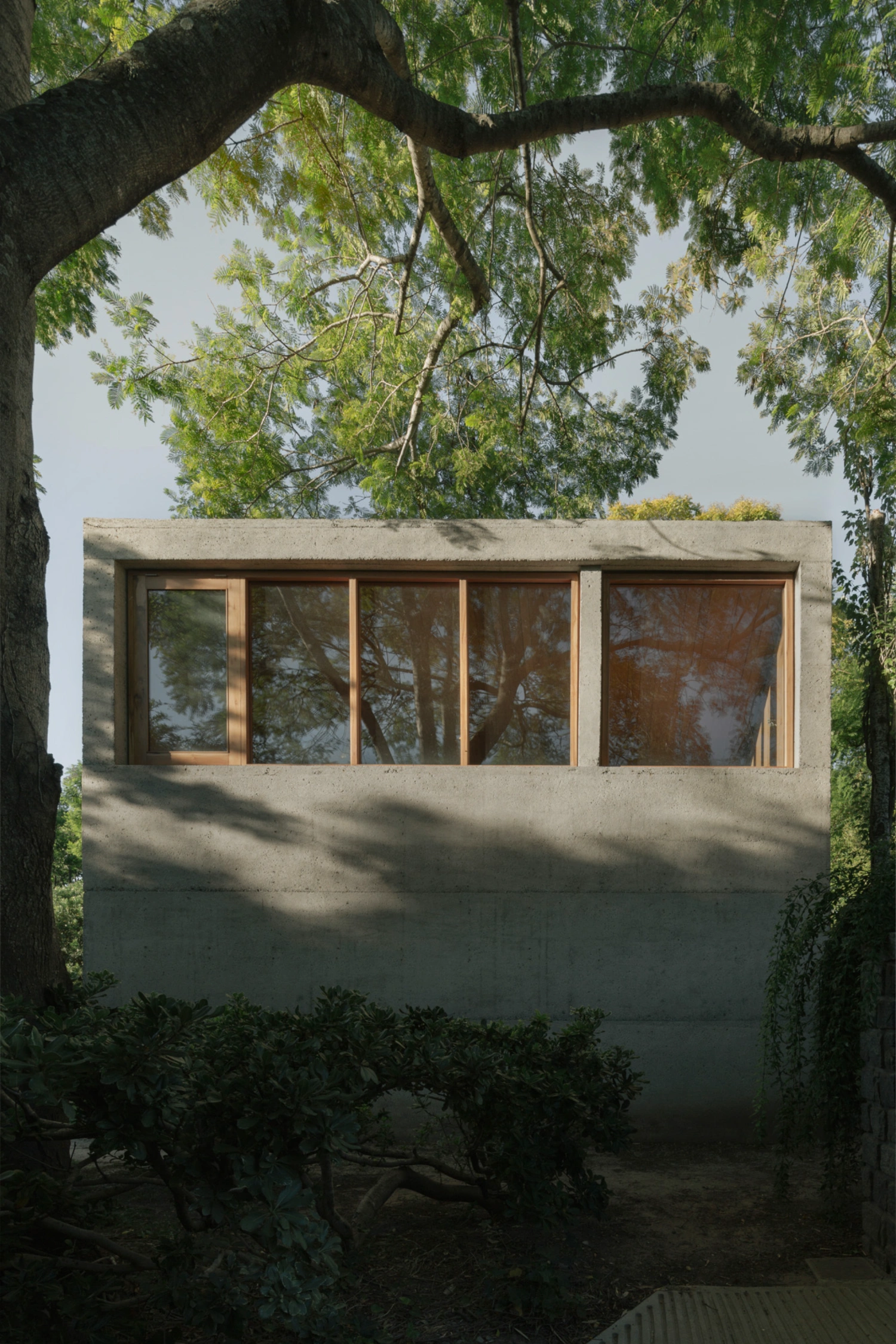 Atelier Workshop by Agustín Berzero — A timber-framed glazing strip punctuates the southern elevation of raw concrete, its warm wood tones contrasting against grey monolithic surfaces.