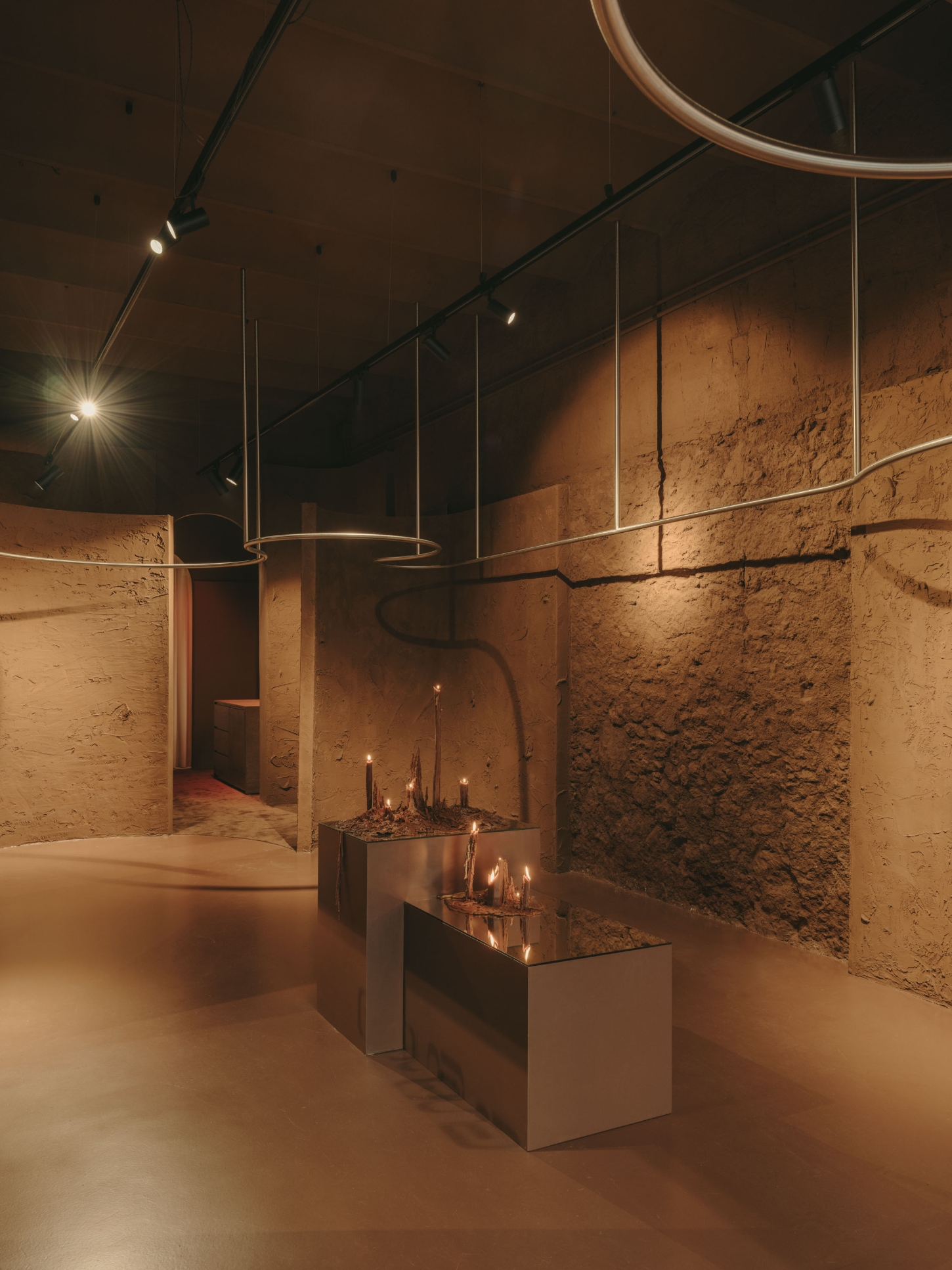 GN0 store by Cristina Cirera — The retail interior unfolds as a series of earthen-toned rooms defined by rammed-earth walls displaying visible tool marks and surface striations.