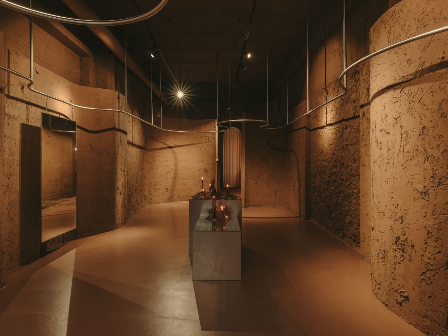 GN0 store by Cristina Cirera — A retail interior defined by rammed-earth walls with pronounced surface irregularities and visible tool marks, extending continuously across both sides of...