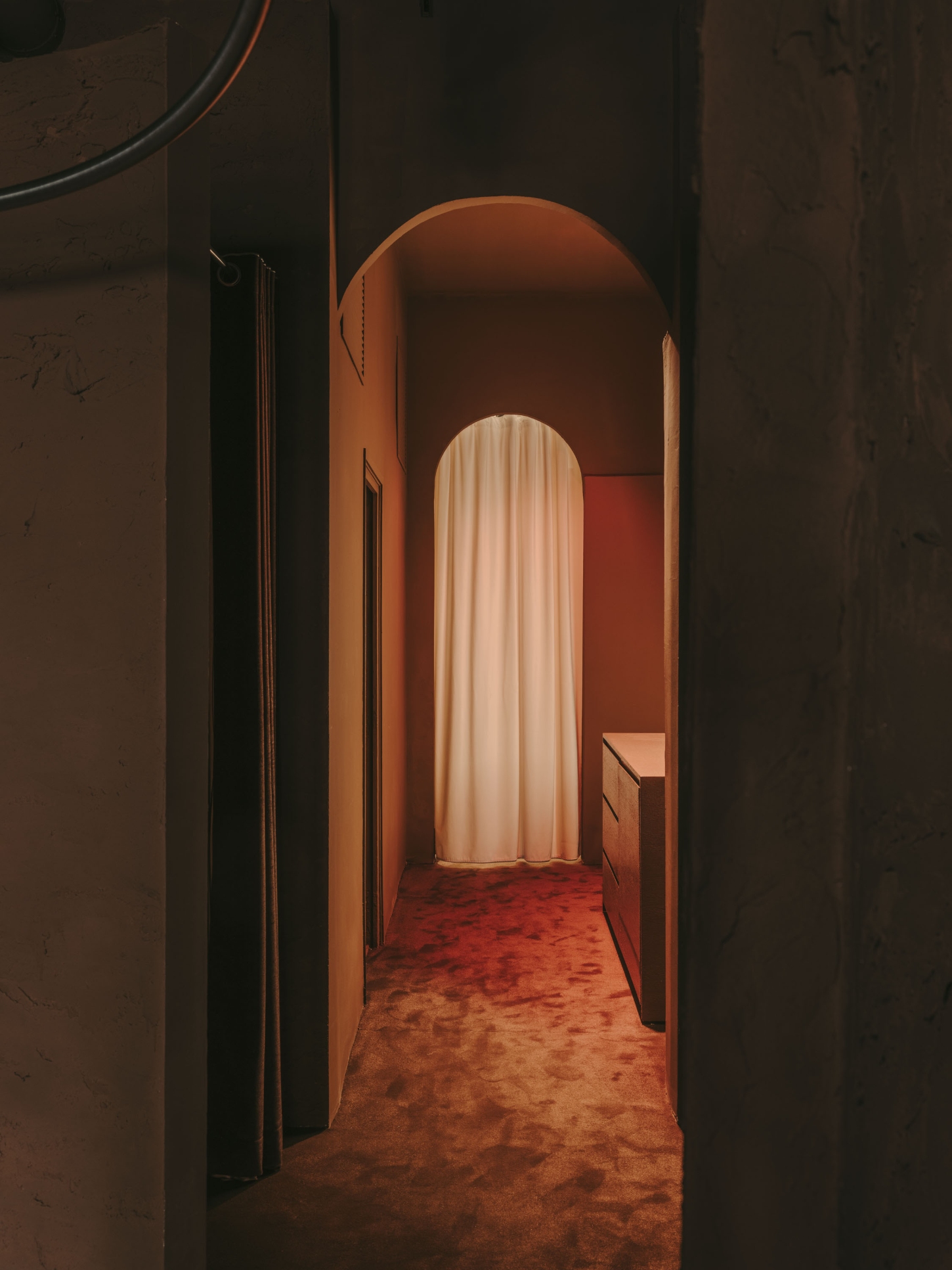 GN0 store by Cristina Cirera — A corridor lined with rammed-earth plaster walls in burnt orange and terracotta tones extends toward a sculptural archway.