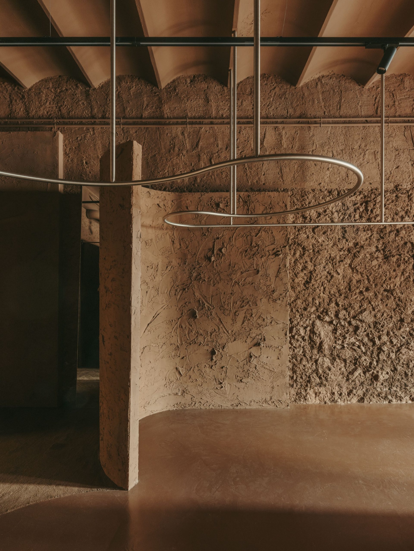 GN0 store by Cristina Cirera — A close-up view of the GN0 store's retail infrastructure reveals the serpentine stainless steel rail system suspended within a gridded metal ceiling framework.