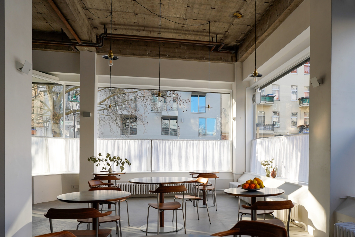 Julius in Berlin — Julius's dining room in Wedding presents a restrained spatial composition anchored by three round walnut tables positioned across a polished concrete floor.