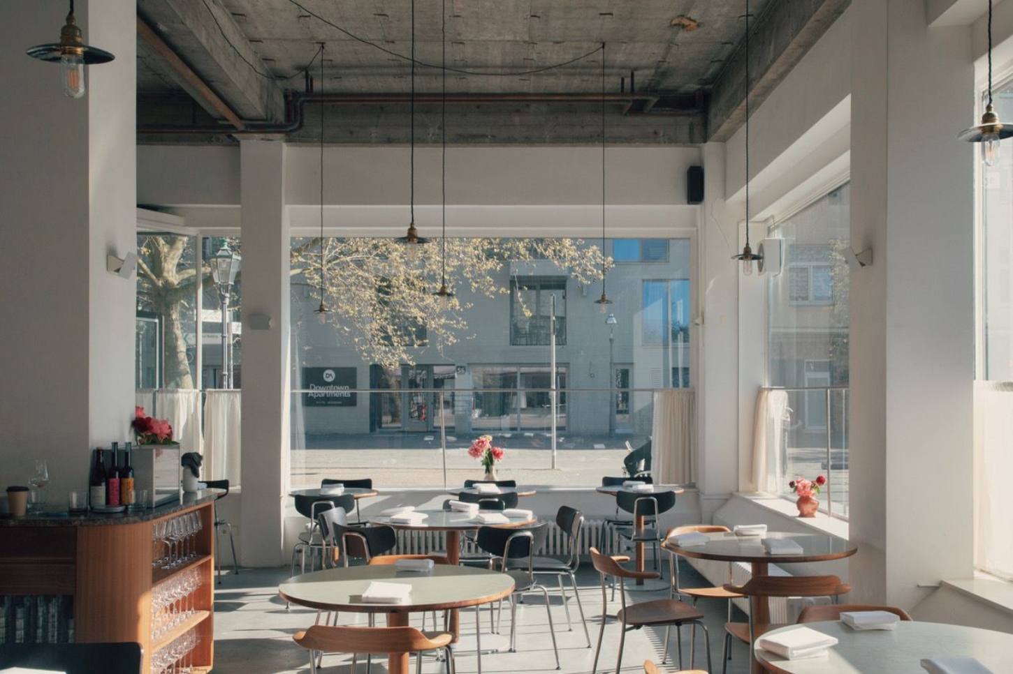 Julius in Berlin — Julius dining room frames the street through floor-to-ceiling glazing, with white linen curtains positioned at mid-height to mediate the boundary between...