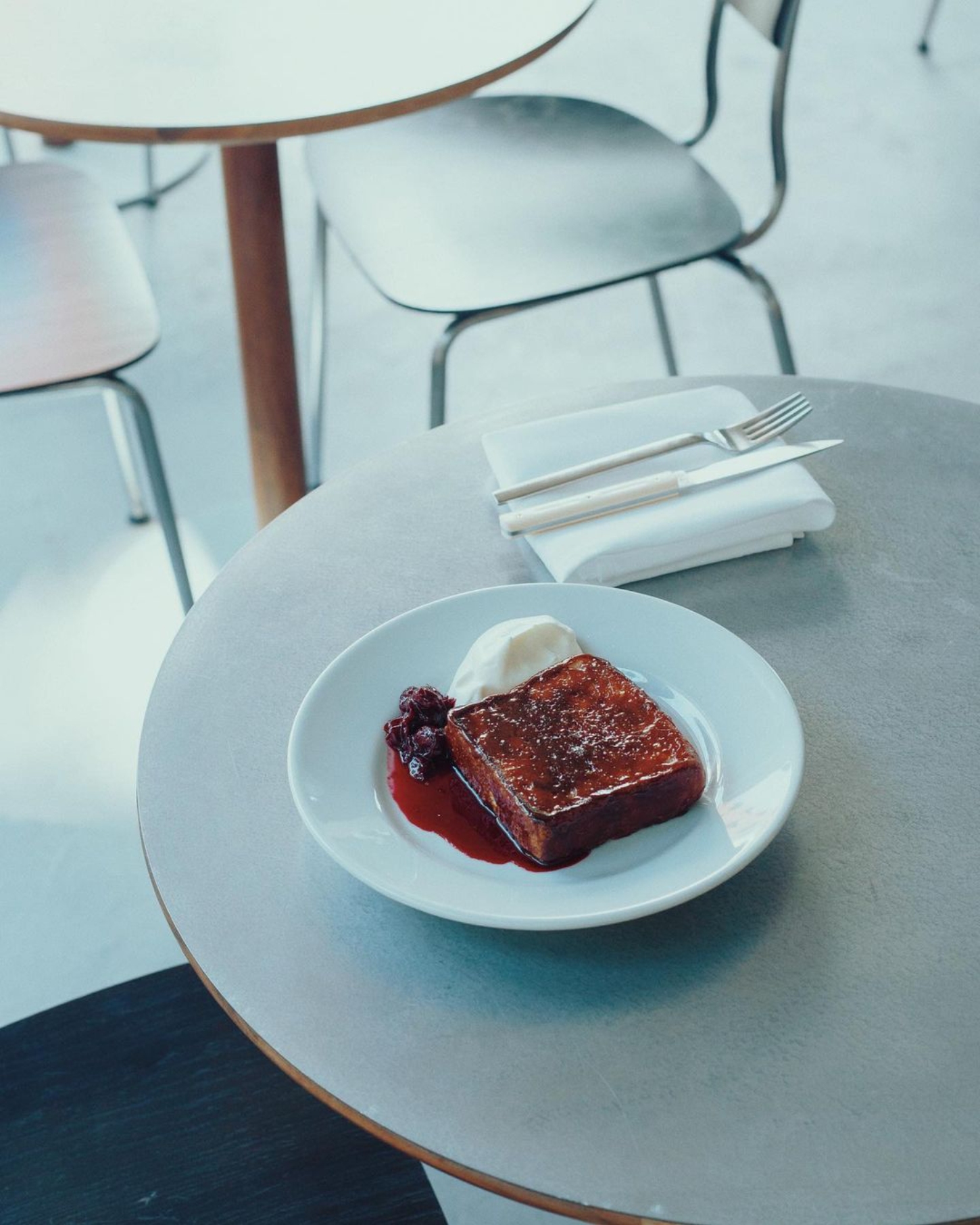 Julius in Berlin — A single place setting at a walnut round table showcases a chocolate cake with berry compote and whipped cream, plated on white ceramic.