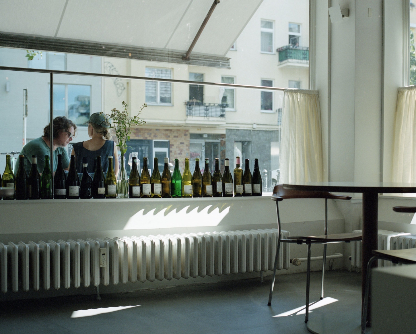 Julius in Berlin — A wine tasting setup dominates the foreground of Julius's dining room, with approximately twenty bottles arranged in a precise linear sequence along the...