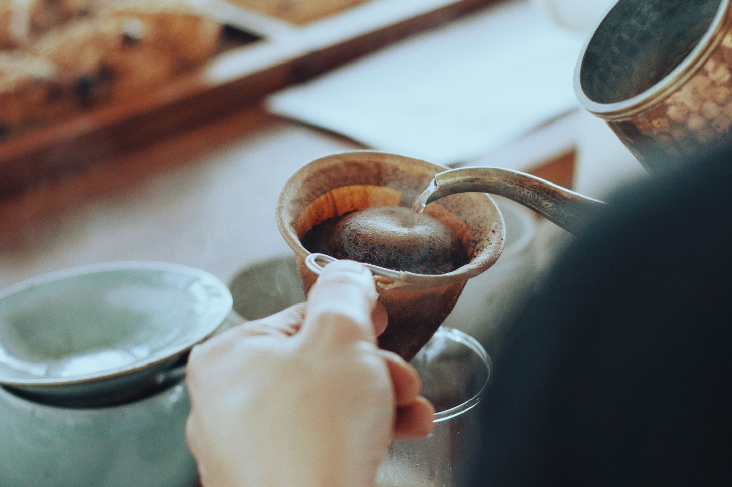 Julius in Berlin — A close-up detail of table service at Julius, capturing a hand holding a ceramic bowl filled with dark liquid, its interior glazed in warm terracotta tones.